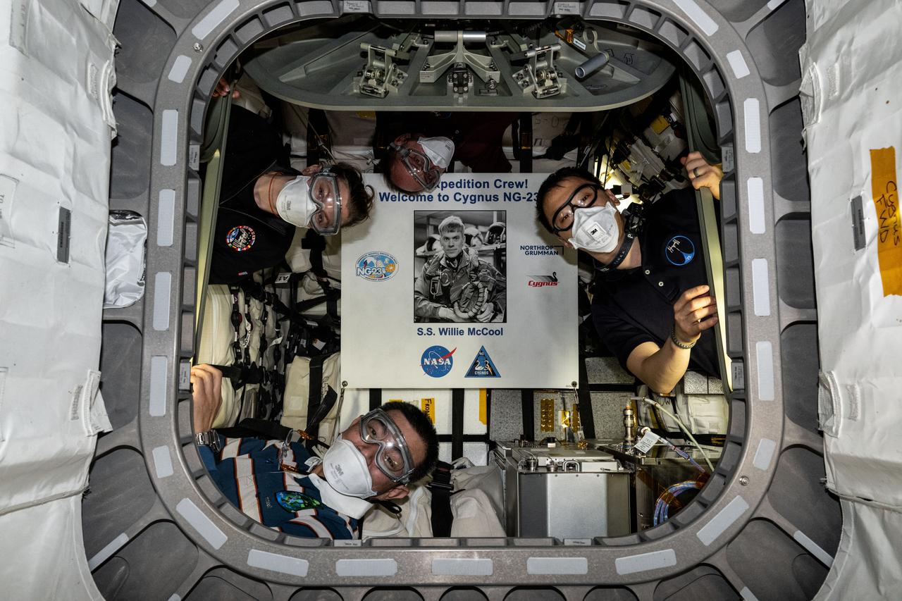 iss073e0704080 (Sept. 18, 2025) --- Pictured inside the Northrop Grumman Cygnus XL cargo craft are (clockwise from left) Flight Engineers Zena Cardman, Mike Fincke, and Jonny Kim of NASA, and Flight Engineer Kimiya Yui of JAXA (Japan Aerospace Exploration Agency). The four astronauts are wearing personnel protective equipment as is standard protocol to shield their eyes and lungs from potential dust and debris that may have been dislodged during Cygnus launch to the International Space Station. Highlighted at center, is a poster of William “Willie” McCool, in honor of the NASA astronaut who perished in 2003 during the space shuttle Columbia accident and for whom the Cygnus spacecraft is named.
