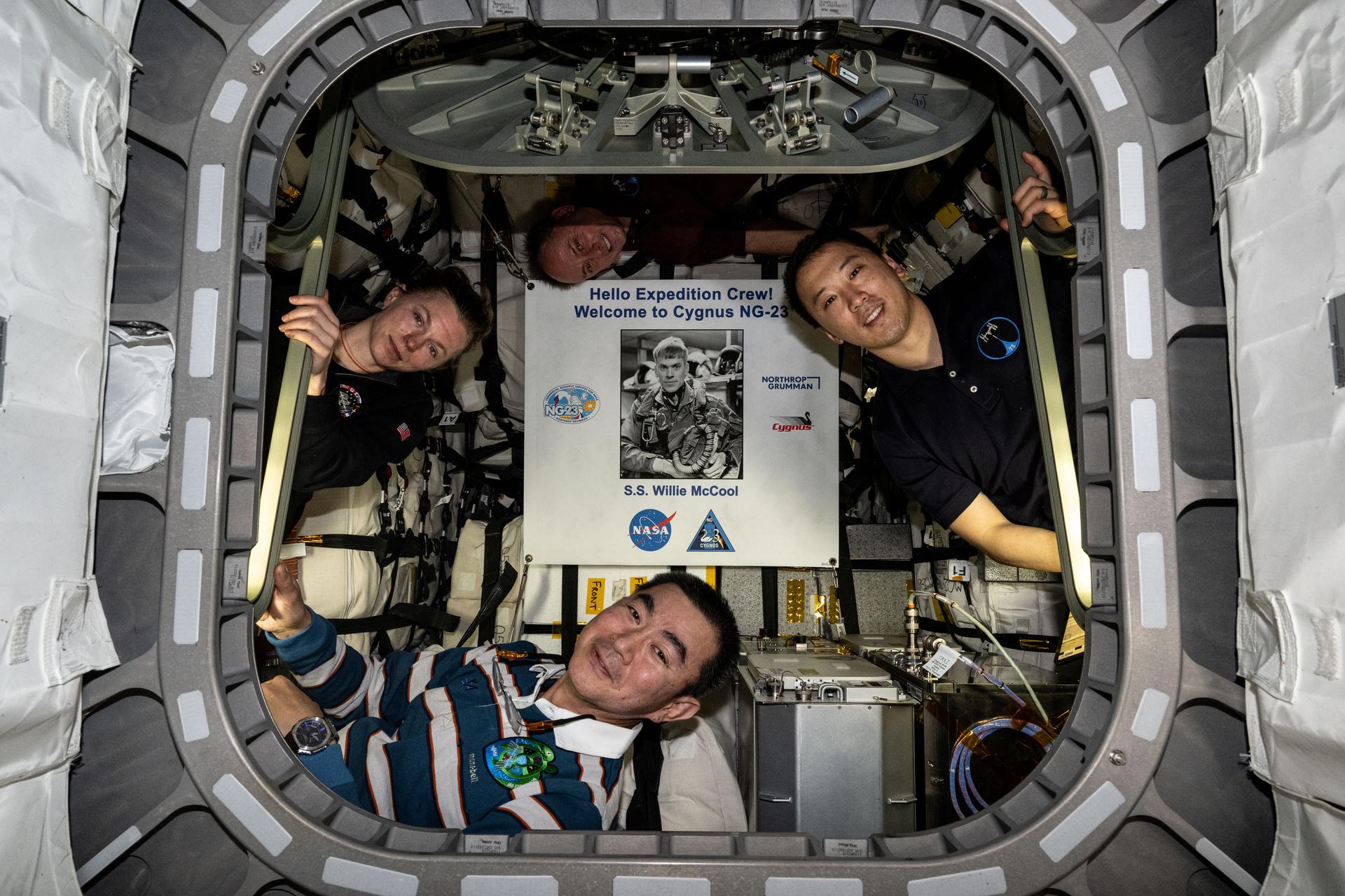 Pictured inside the Northrop Grumman Cygnus XL cargo craft are (clockwise from left) Flight Engineers Zena Cardman, Mike Fincke, and Jonny Kim of NASA, and Flight Engineer Kimiya Yui of JAXA (Japan Aerospace Exploration Agency). Highlighted at center, is a poster of William “Willie” McCool, in honor of the NASA astronaut who perished in 2003 during the space shuttle Columbia accident and for whom the Cygnus spacecraft is named.