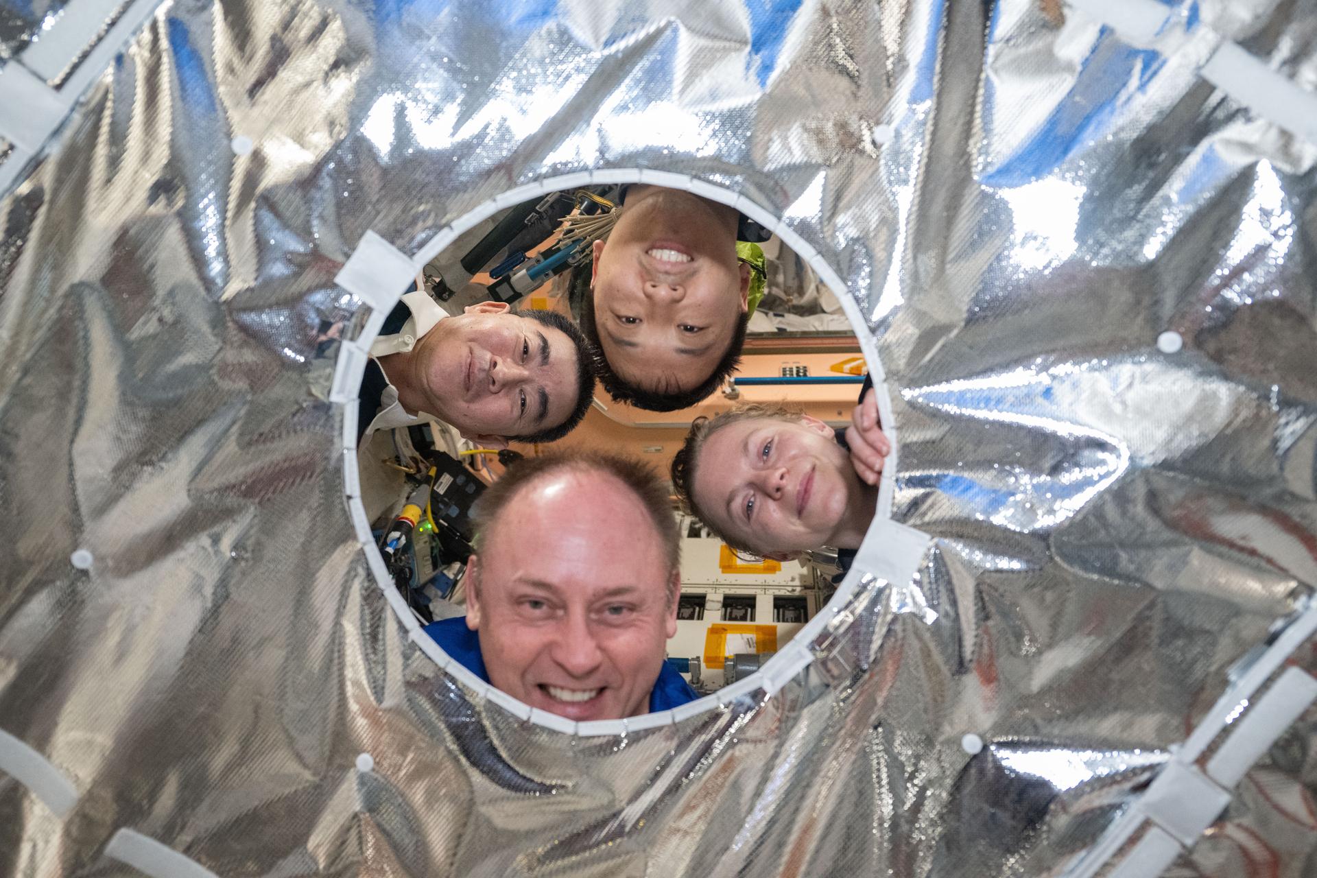 Four Expedition 73 flight engineers pose for a playful portrait through a circular opening in a hatch thermal cover aboard the International Space Station. The cover provides micrometeoroid and orbital debris protection while maintaining cleanliness and pressure integrity in the vestibule between Northrop Grumman's Cygnus XL cargo spacecraft and the orbital outpost. The opening allows for visual inspection of hatch alignment, access to the hatch handle or pressure equalization valve, and visibility for sensors or cameras during berthing operations. Clockwise from left, are JAXA (Japan Aerospace Exploration Agency) astronaut Kimiya Yui and NASA astronauts Jonny Kim, Zena Cardman, and Mike Fincke.