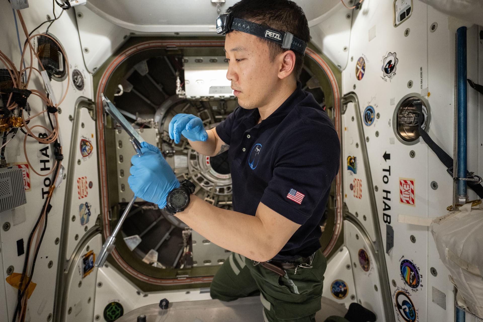 NASA astronaut and Expedition 73 Flight Engineer Jonny Kim reviews procedures on a computer tablet before opening the hatch to the Cygnus XL cargo spacecraft from Northrop Grumman. He was preparing to open Cygnus' hatch to begin unloading about 11,000 pounds of new science and supplies for the Expedition 73 crew.