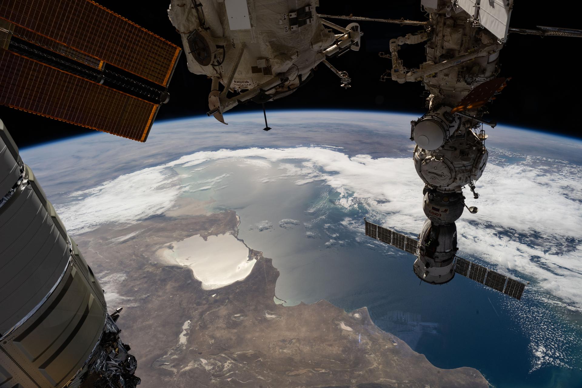 The Caspian Sea and the hypersaline Garabogazköl Basin (center left) are visible below the International Space Station as it orbited 263 miles above western Kazakhstan. In the right foreground, the Soyuz MS-27 crew spacecraft is docked to the Prichal module. At the top center, the lower portion of the Rassvet module is visible, while the left side of the frame shows part of the Northrop Grumman Cygnus XL cargo spacecraft.