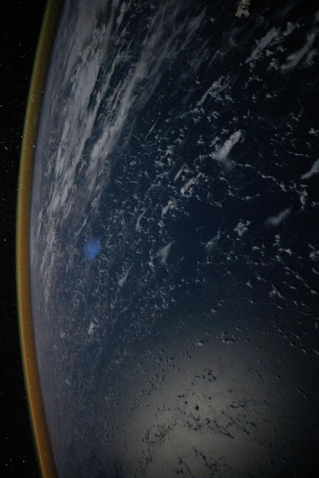 A red-yellow airglow blankets Earth's horizon above the tranquil, moonlit Philippine Sea in this photograph taken from the International Space Station at approximately 1:49 a.m. local time while orbiting 261 miles above Earth. This type of airglow is caused by chemical reactions in the upper atmosphere, often involving oxygen and hydroxyl molecules, and is typically visible in long-exposure imagery taken from orbit.