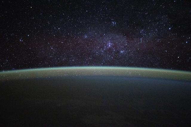 NASA image: Stars fill the sky above a serene, blue-green airglow blanketing Earth's horizon