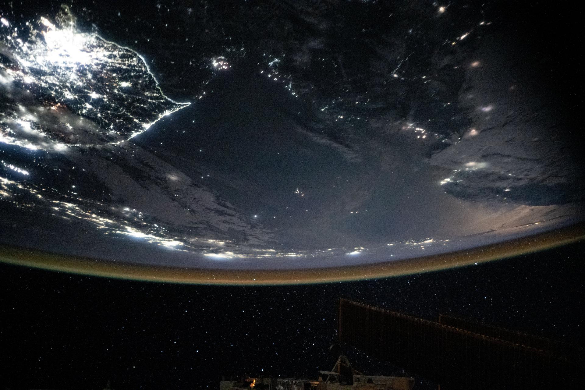 At top left, the bright lights of the Korean Peninsula abruptly end at the border between South Korea and North Korea highlighting stark differences in energy infrastructure. The Seoul Capital Area—comprised of Seoul, Incheon, and Gyeonggi Province, and home to over 25 million people—is prominent in this nighttime image. Japan stretches across the center of the frame near Earth’s horizon, illuminated beneath a red-yellow airglow. The International Space Station was orbiting 262 miles above Earth at approximately 12:55 a.m. local time when this photograph was taken.