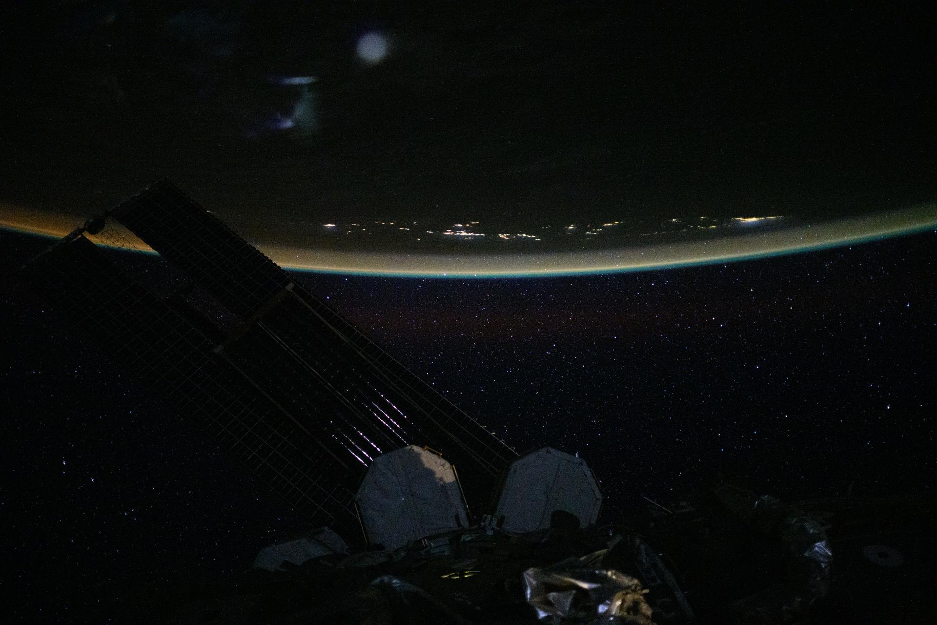 This serene, nighttime view from the International Space Station, captured from an altitude of 262 miles above the Coral Sea, reveals a star-filled sky with a soft, multi-colored atmospheric glow blanketing the city lights of the Solomon Islands. The image was taken at approximately 3:11 a.m. local time as the station orbited above the southwestern Pacific region.