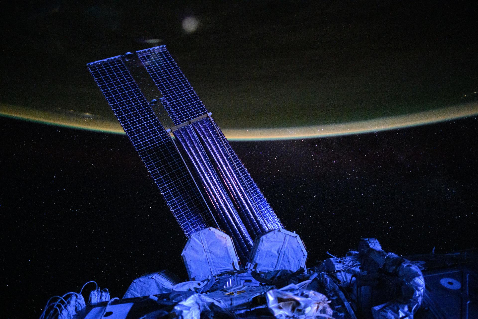 This moonlit, violet-hued view of the International Space Station’s main solar arrays, partially overlapped by a smaller set of roll-out solar arrays, was captured at approximately 5:16 a.m. local time. The orbital outpost was soaring 265 miles above the Pacific Ocean, just north of New Zealand, when this photograph was taken.