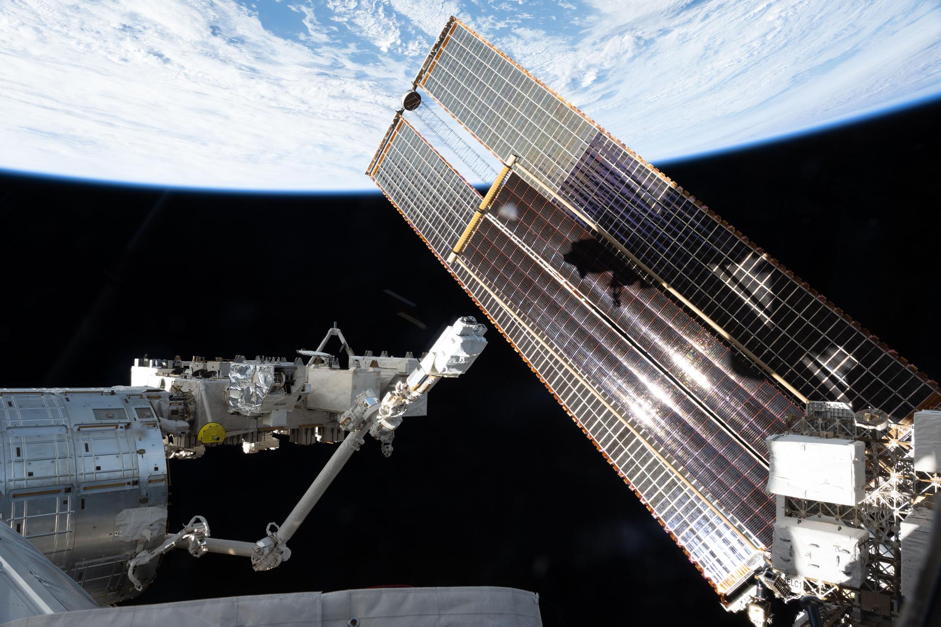 A set of the International Space Station's main solar arrays, partially overlapped by a smaller set of roll-out solar arrays, stretches across the photograph as the International Space Station orbited 262 miles above the Atlantic Ocean off the coast of Portugal. At left, the Japanese robotic arm with the small satellite orbital deployer attached, extends from the Kibo laboratory module.