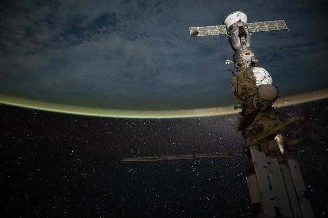 NASA image: A yellow-green airglow blankets Earth’s horizon beneath a star-filled sky