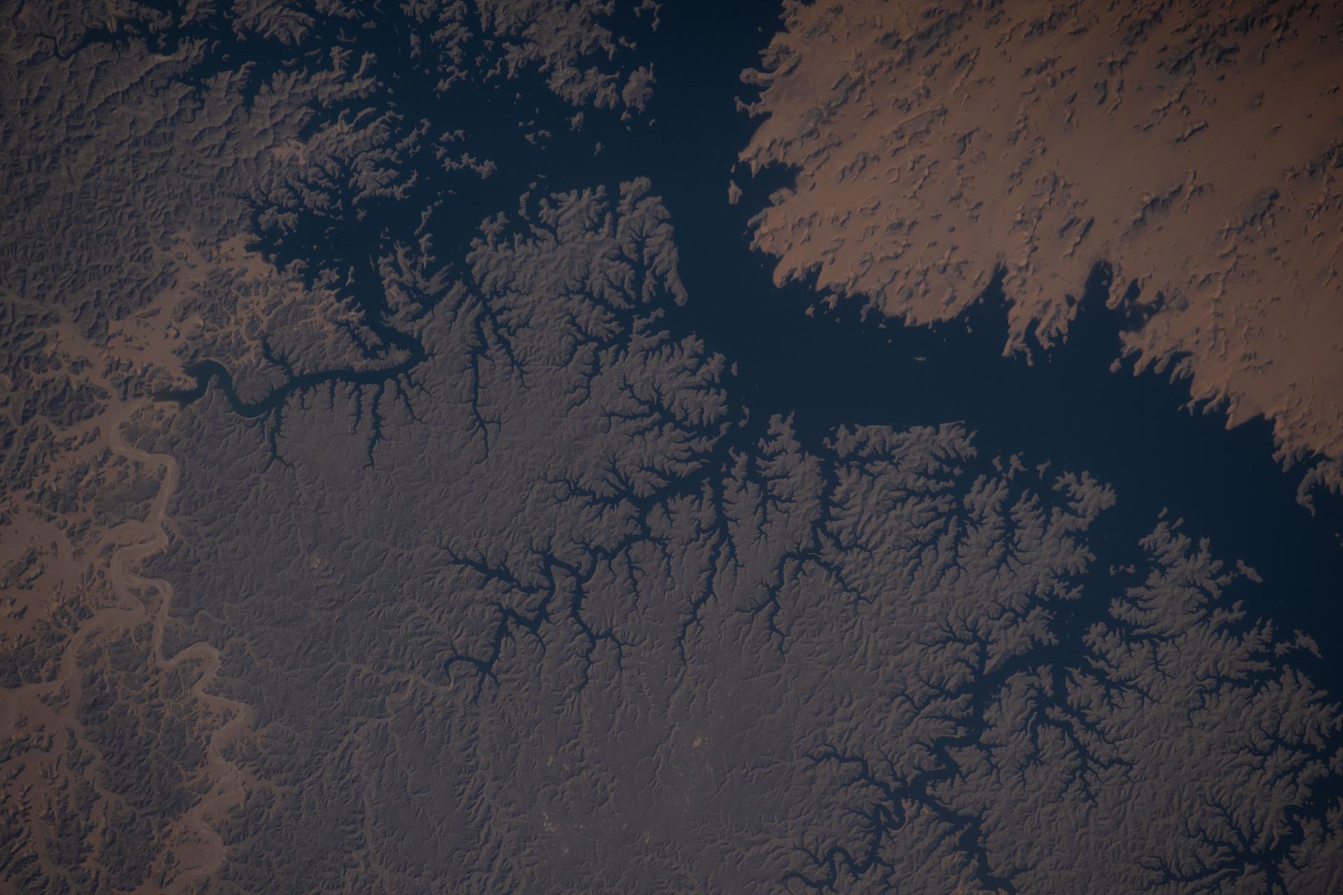 Lake Nasser, created by the Aswan High Dam in southern Egypt, is one of the world’s largest man-made reservoirs. Extending into northern Sudan, it stores water from the Upper Nile and regulates its flow into the Lower Nile. This photograph was taken from the International Space Station while orbiting 260 miles above the eastern Sahara.