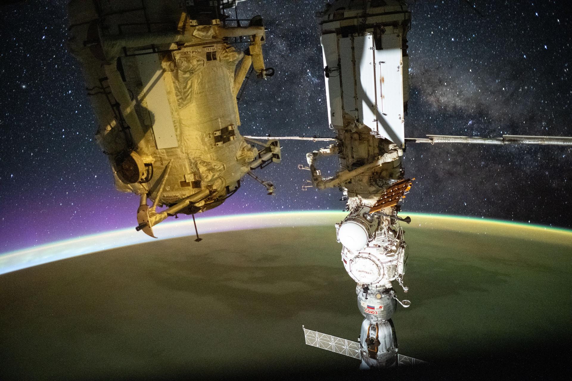 iss073e0880390 (Oct. 13, 2025) --- This long-exposure photograph captures a yellow-green airglow blanketing Earth as an orbital sunrise begins to illuminate the planet’s upper atmosphere. The Milky Way stretches across the star-filled night sky in the background, while the golden-hued Rassvet module and the Soyuz MS-27 crew spacecraft—docked to the Prichal module, itself attached to the Nauka science module—dominate the foreground. The International Space Station was orbiting 268 miles above the South Atlantic Ocean at approximately 2:45 a.m. local time when this photograph was taken.