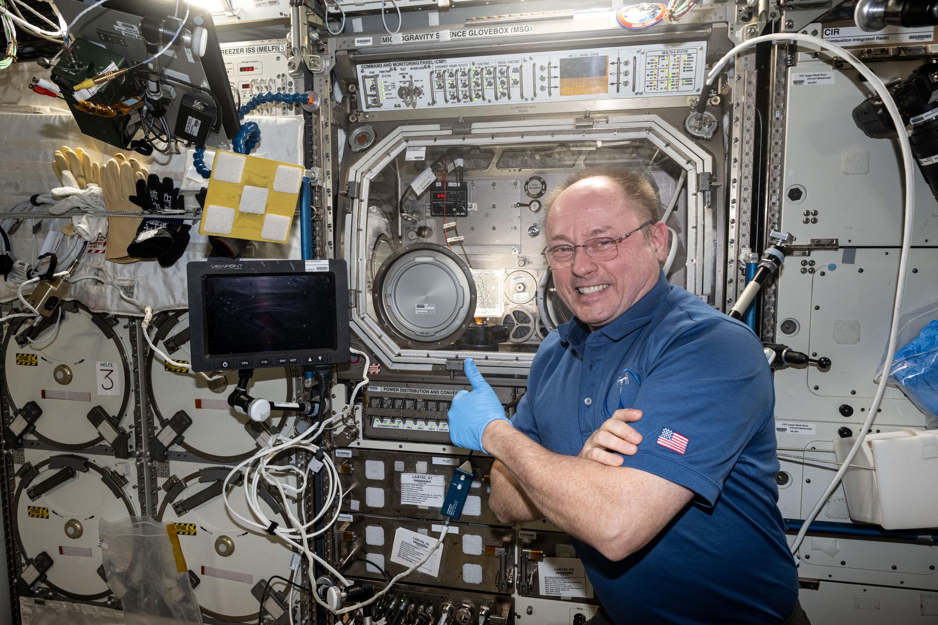 NASA astronaut and Expedition 73 Flight Engineer Mike Fincke gives a thumbs-up in front of the Microgravity Science Glovebox (MSG) inside the International Space Station's Destiny laboratory module. Fincke had just completed research operations for the Fluid Particles experiment, which helps researchers understand how particles in a liquid interface come together to form larger structures or clusters in microgravity. Results could advance fire suppression, lunar dust control, and plant growth in space. Earth benefits may include insights into pollen behavior, algae blooms, plastic pollution, and sea salt transfer during storms.
