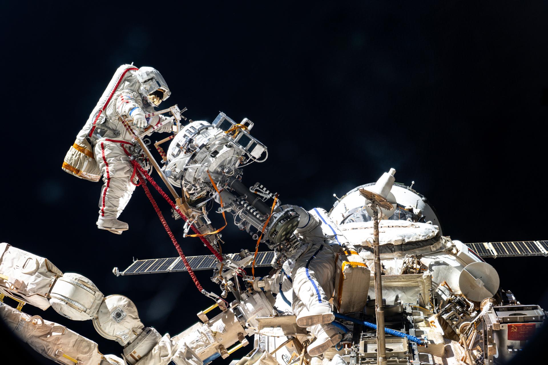 Roscosmos cosmonauts Sergey Ryzhikov (left) and Alexey Zubritsky (bottom right) work together to remove a high-resolution camera (HRC) monoblock during a six-hour and nine-minute spacewalk outside the International Space Station's Roscosmos segment. The HRC monoblock is part of a scientific optical telescope system designed to test compact radio-optical detectors for Earth observation, ecological monitoring, and emergency response.