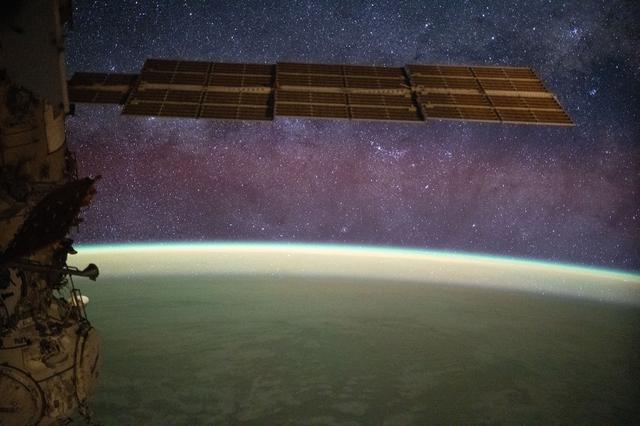 NASA image: The Milky Way spans the night sky above a yellow-green airglow