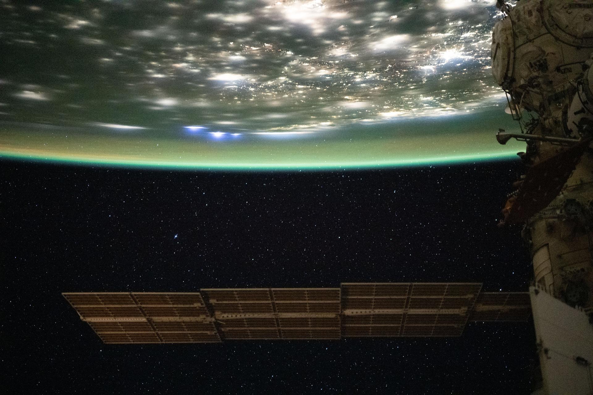 iss073e0982450 (Oct. 25, 2025) --- A blue-green airglow blankets the bright city lights of the eastern United States, with bluish-white lightning strikes visible on Earth's horizon near the center-left of the frame. Stars twinkle in the night sky in the lower half of the image, captured at approximately 2:03 a.m. local time from the International Space Station as it orbited 262 miles above northeastern Pennsylvania.