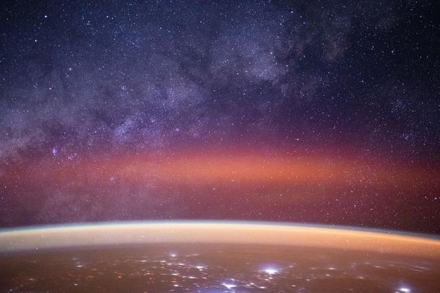 NASA image: The Milky Way spans the night sky above a bright orange-yellow airglow