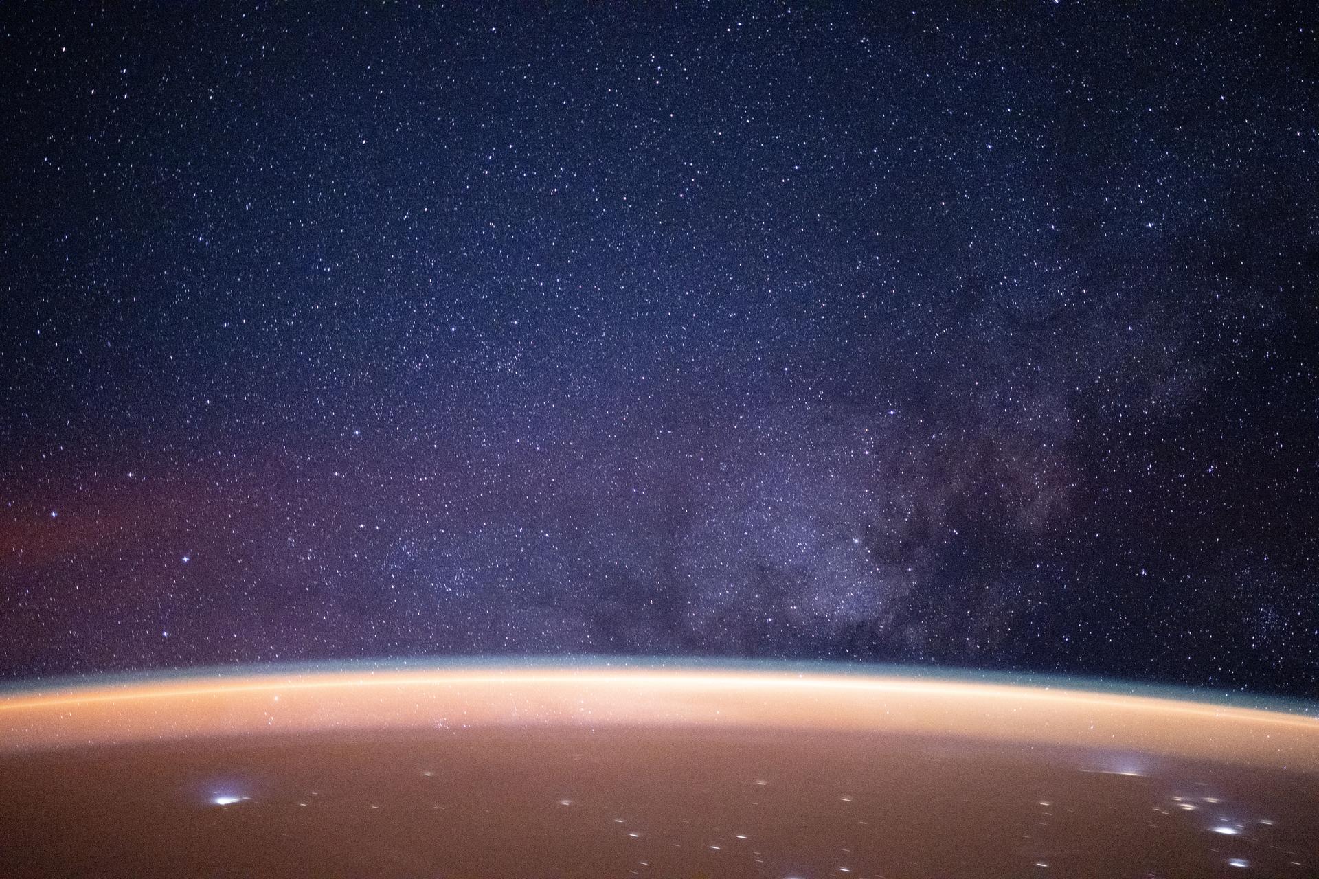 A reddish airglow blankets Earth beneath a star-filled sky illuminated by the Milky Way. The planet’s surface is sparsely dotted with city lights along the desert coast of the Middle East by the Arabian Sea. The International Space Station was orbiting 258 miles above Earth at approximately 11:34 p.m. local time when this photograph was taken.