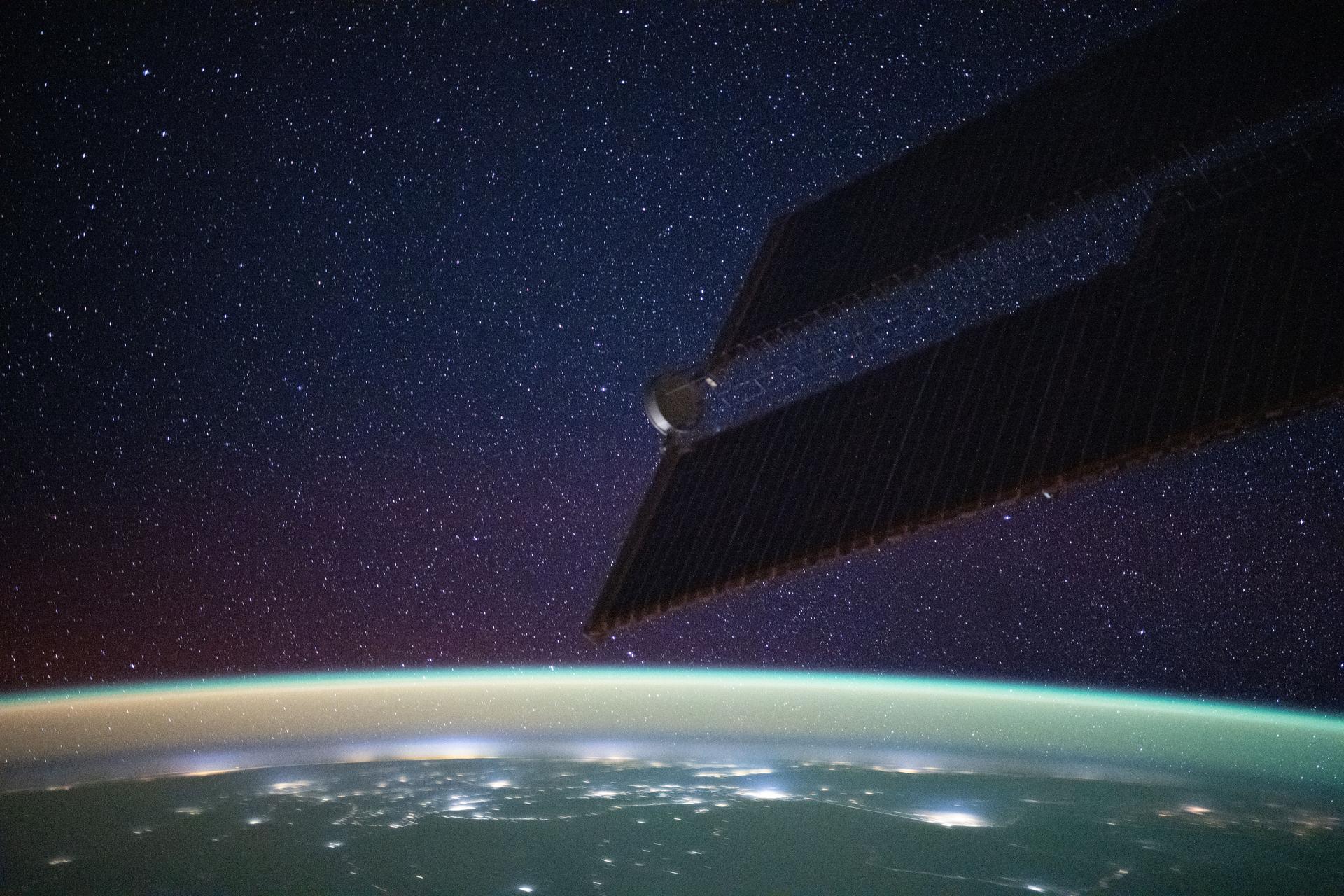 A bright yellow-green airglow blankets Earth's horizon, dotted with the city lights of northern India, beneath a star-filled sky. This long-exposure photograph was taken from the International Space Station as it orbited 260 miles above the Himalayas at approximately 1:11 a.m. local time.