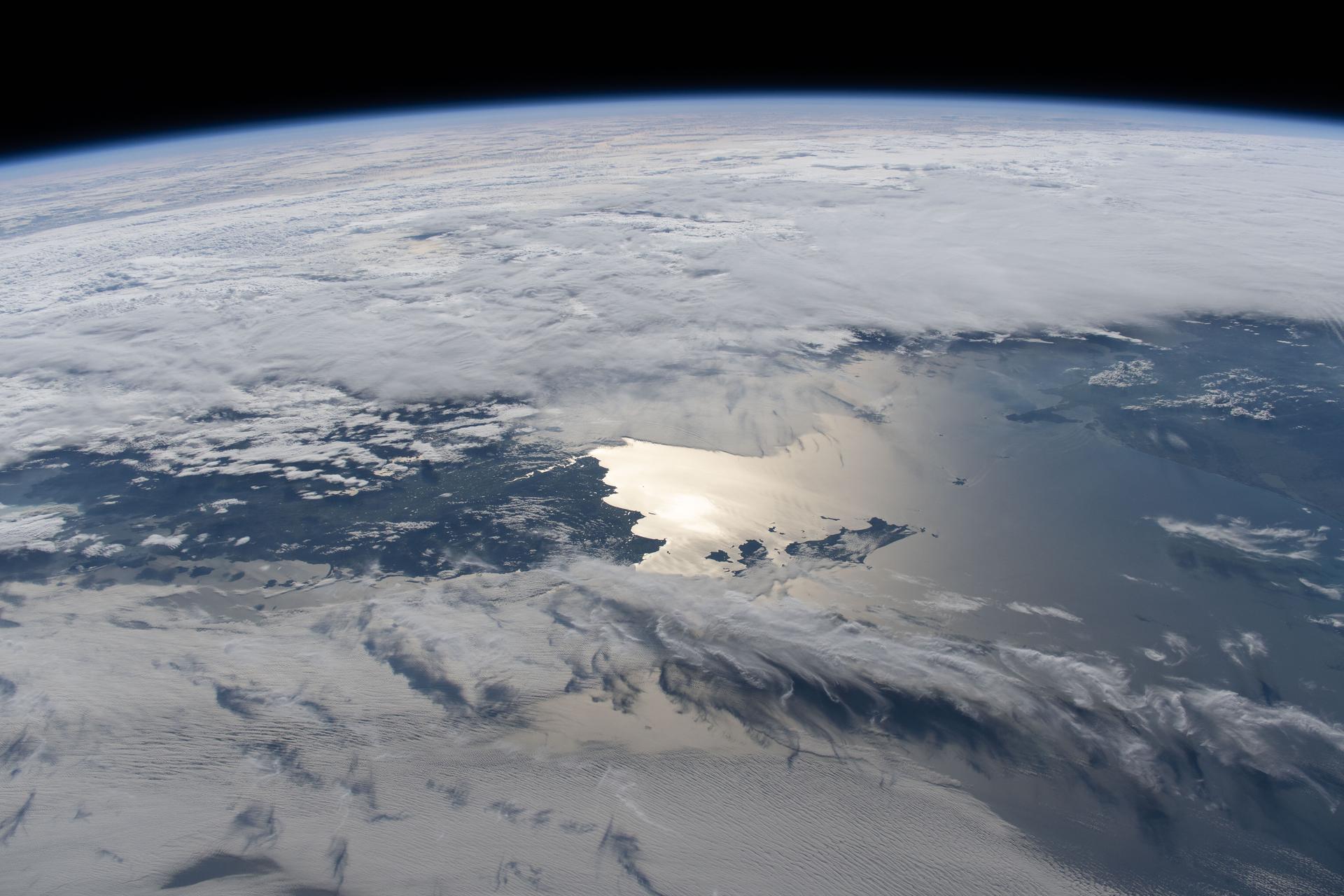 Clouds surround Australia's island state of Tasmania, highlighting its northern region as sunlight glints off the Bass Strait. The sun’s reflection also reveals the Tamar River, which leads to Launceston—one of Australia’s oldest cities—renowned for its vibrant food and wine culture and a metropolitan population of over 91,000.