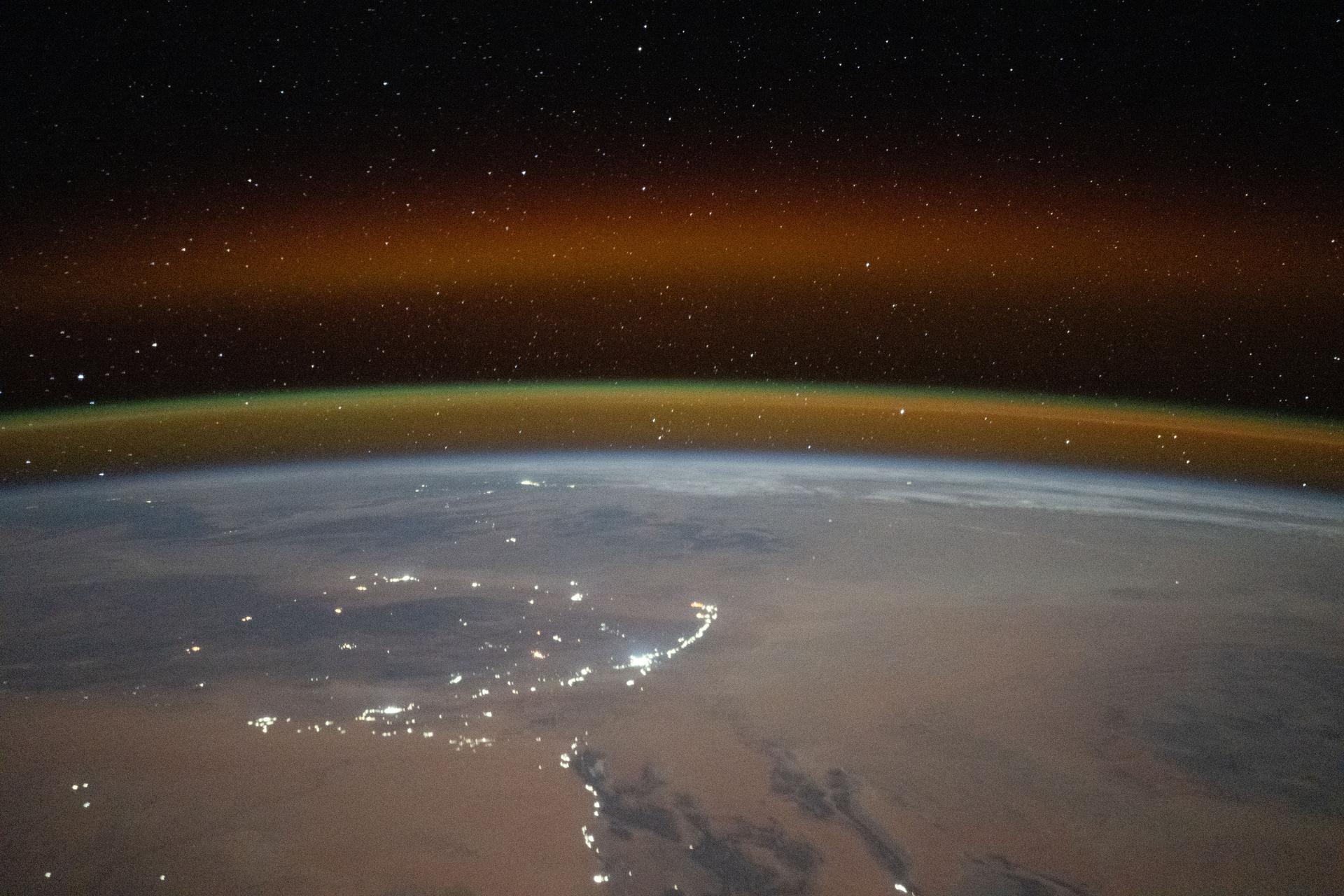 A yellow-red airglow blankets Earth's horizon as village lights dot the Saharan landscape of Algeria in this photograph taken at approximately 8:50 p.m. local time from the International Space Station as it orbited 261 miles above north Africa.