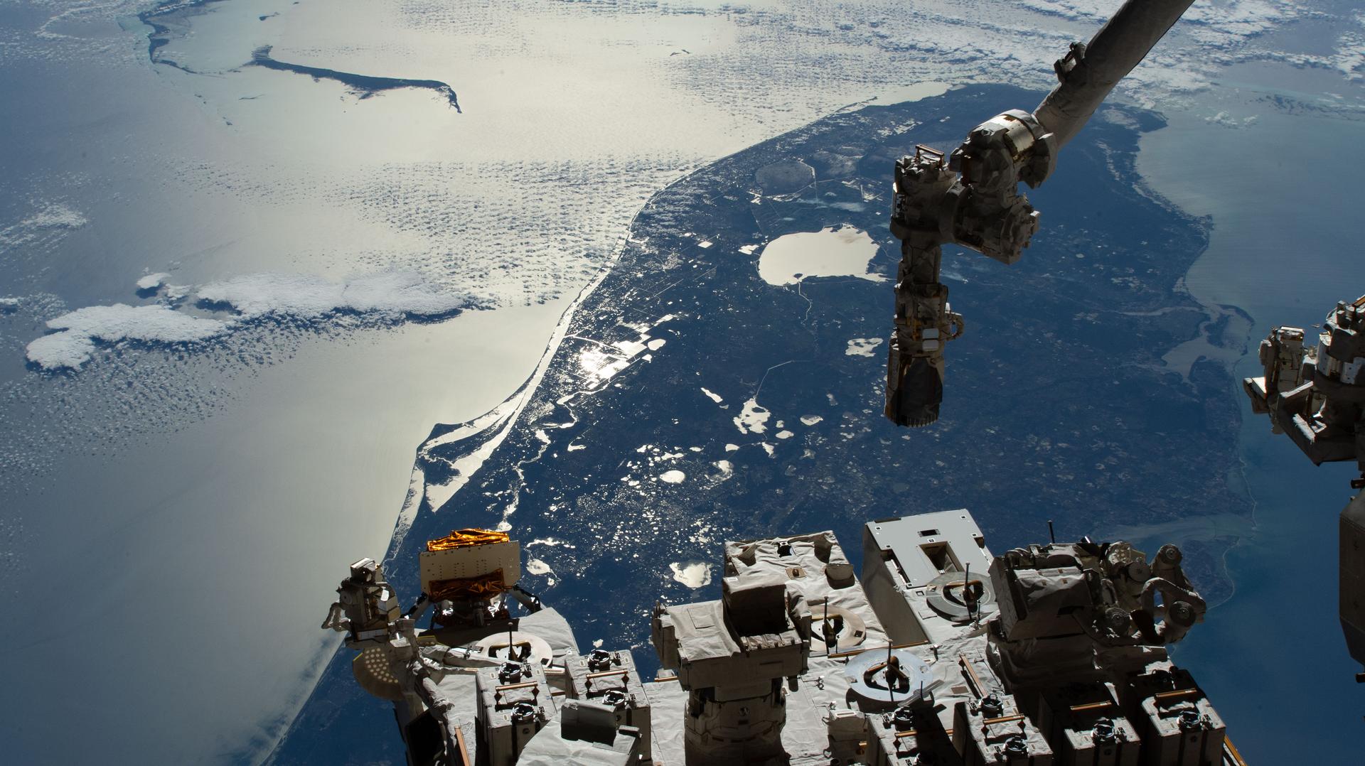 The sun’s glint beams off the Atlantic Ocean, contrasting with southern Florida and a portion of the Bahamas (upper left) in this photograph taken from the International Space Station as it orbited 262 miles above the southeastern United States. In the bottom foreground is the Kibo laboratory module’s Exposed Facility, which hosts a variety of experiment payloads and other hardware exposed to the external microgravity environment. Extending from the top right of the frame is the Japanese robotic arm, which can maneuver payloads into and out of Kibo’s airlock for placement on the Exposed Facility.