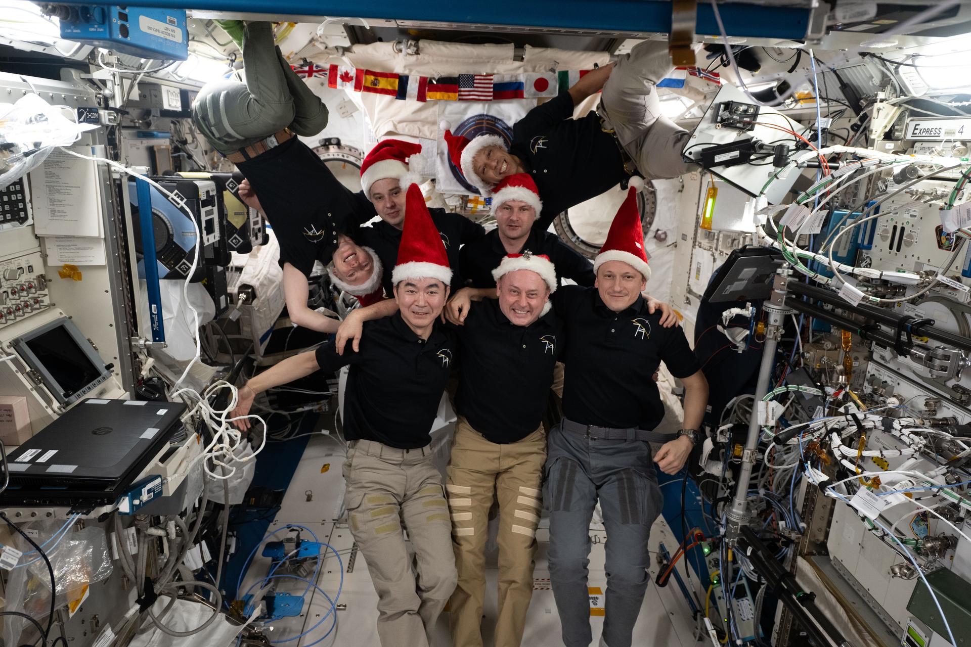The seven-member Expedition 74 crew poses for a festive portrait aboard the International Space Station's Kibo laboratory module. In the front row, from left, are Kimiya Yui of JAXA (Japan Aerospace Exploration Agency), Mike Fincke of NASA, and Sergey Kud-Sverchkov of Roscosmos. In the back are, Zena Cardman of NASA, Oleg Platonov of Roscosmos, Chris Williams of NASA, and Sergei Mikaev of Roscosmos.