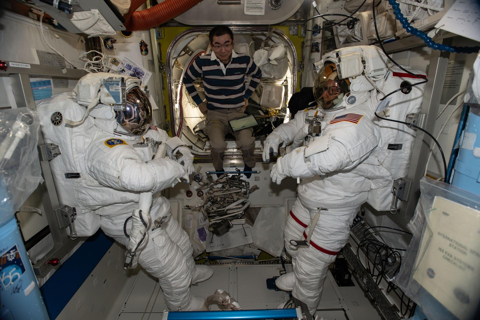 At center, JAXA (Japan Aerospace Exploration Agency) astronaut and Expedition 74 Flight Engineer Kimiya Yui assists NASA astronauts Zena Cardman (left) and Mike Fincke (right), the station’s flight engineer and commander respectively, during spacesuit checks inside the International Space Station’s Quest airlock.