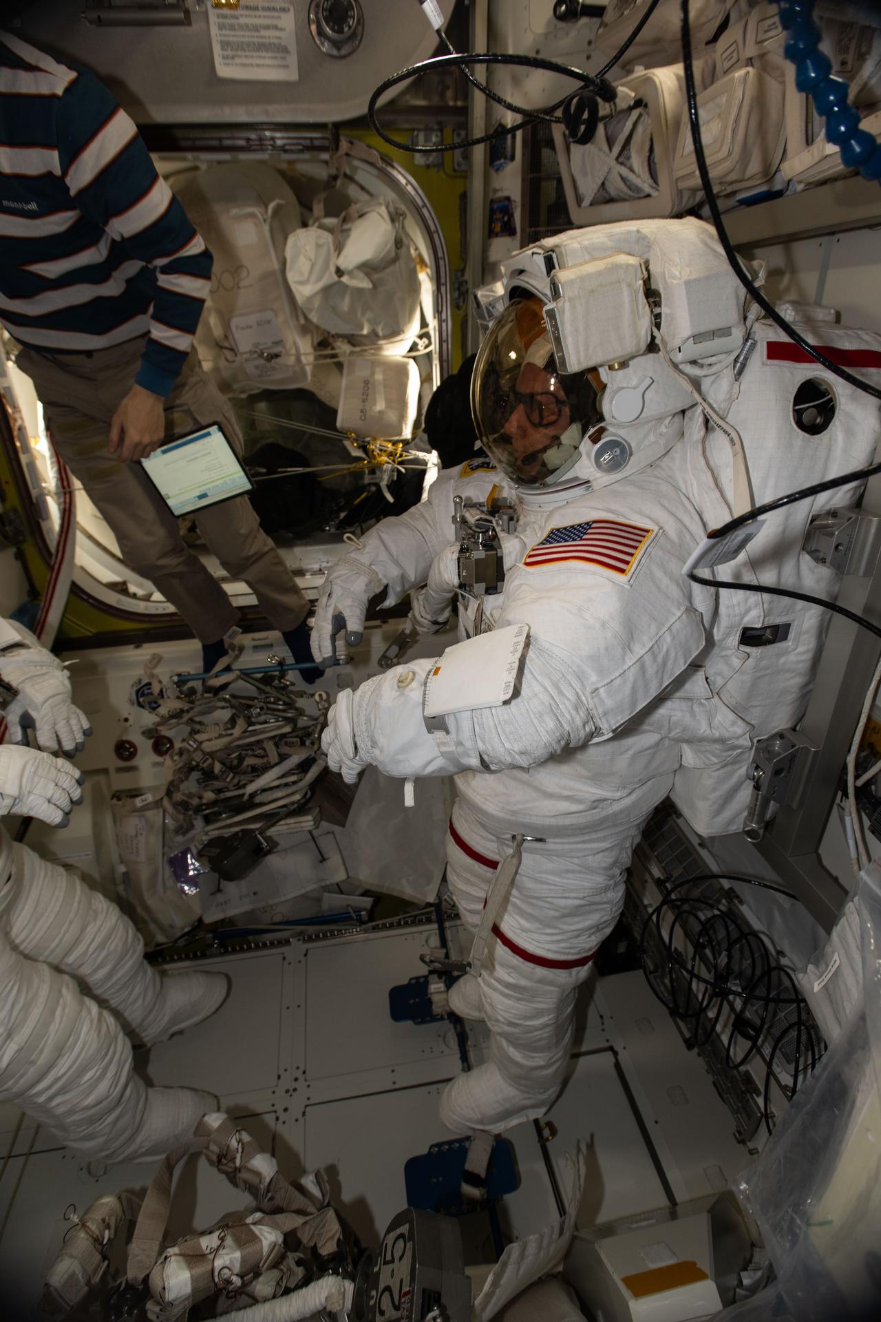 NASA astronaut and Expedition 74 Commander Mike Fincke is pictured in his pressurized spacesuit, checking its communication and power systems ahead of a spacewalk planned for Thursday, Jan. 8, 2025. Partially obscured at left, JAXA (Japan Aerospace Exploration Agency) astronaut and Flight Engineer Kimiya Yui assists NASA Flight Engineer Zena Cardman as she tests the operations of her spacesuit inside the International Space Station’s Quest airlock.