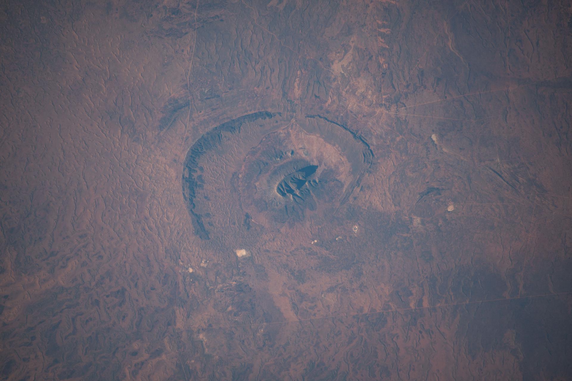 Mount Conner, in the arid heart of Australia’s Northern Territory—also known as the Red Centre—is a flat-topped mesa and an erosional remnant whose distinct formation took shape approximately 100 million years ago. It resembles an impact crater because it sits on a broad, eroded plain with shallow depressions, while the surrounding terrain was shaped by millions of years of weathering and erosion. The International Space Station was orbiting 262 miles above the island continent when this photograph was taken.