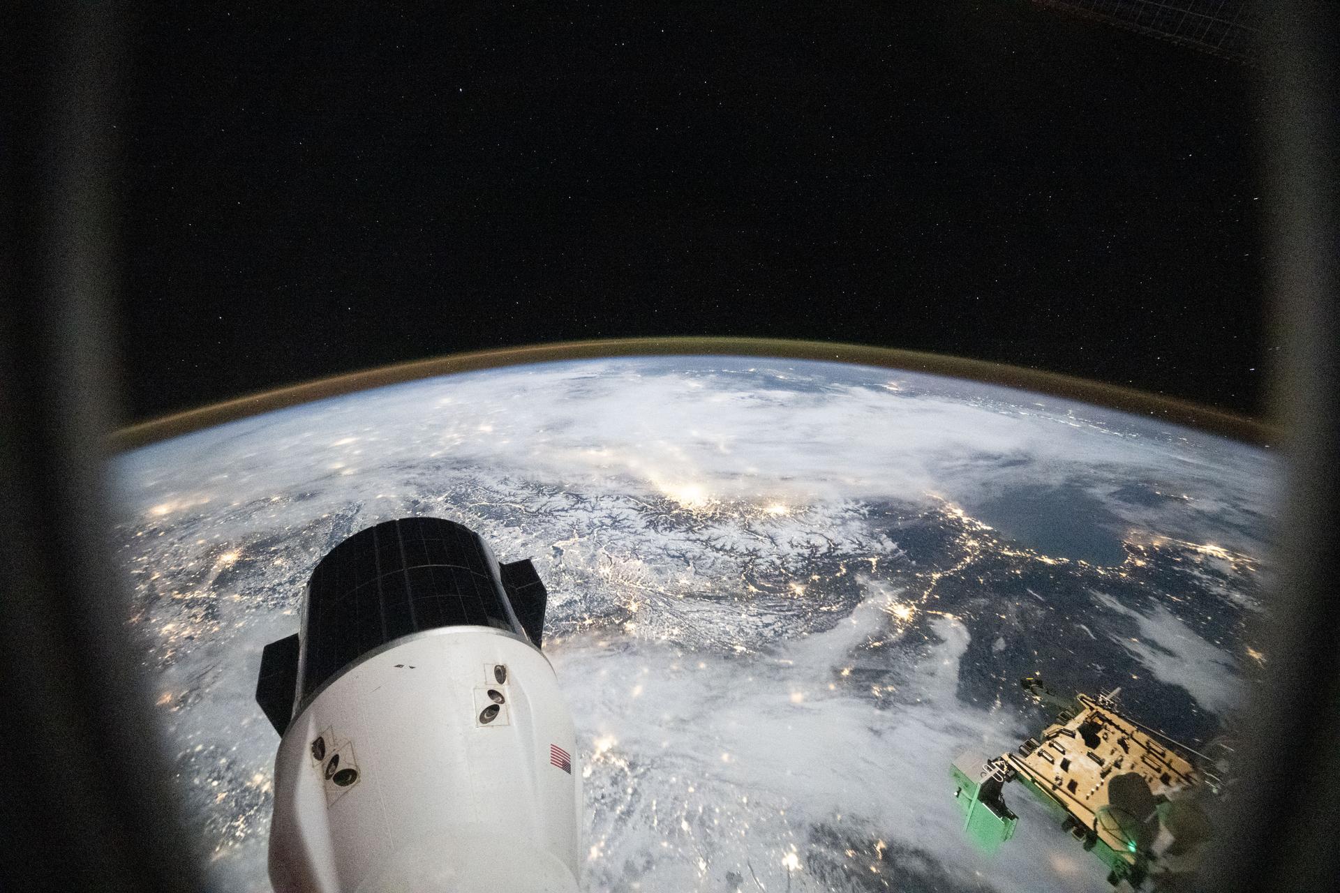 iss074e0224384 (Jan. 6, 2026) --- City lights sparkle across a cloudy Europe and the Alps in this photograph from a window on a SpaceX Dragon crew spacecraft as the International Space Station orbited 266 miles above Germany at approximately 2:37 a.m. local time. In the foreground, is another SpaceX Dragon spacecraft. Credit: JAXA/Kimiya Yui