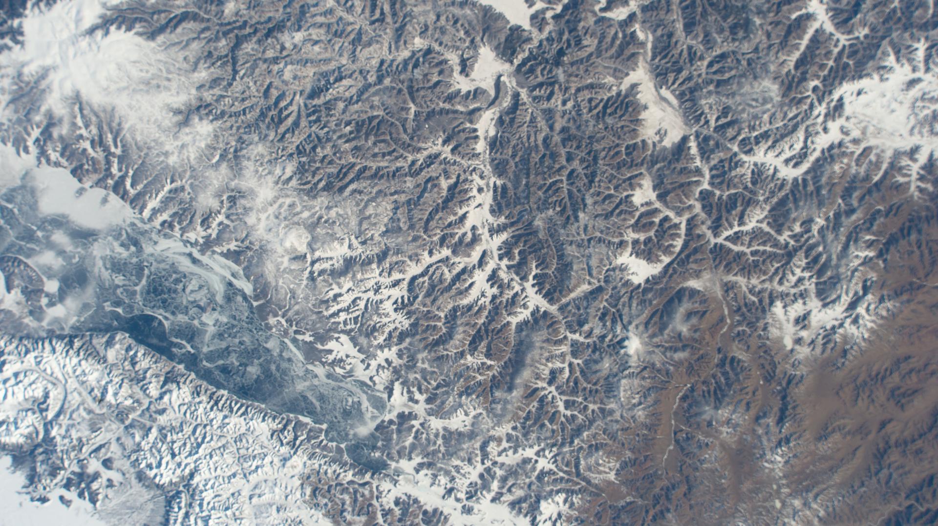 The frozen Khuvsgul Lake (left) in Mongolia appears hidden within the wintry landscape of the Siberian Taiga near the Russian border—the largest terrestrial biome on Earth, characterized by rugged mountain ranges, forested hills, and meadows, and home to wildlife such as brown bears, wolves, moose, and reindeer. The International Space Station was orbiting 261 miles above Asia when this photograph was taken.