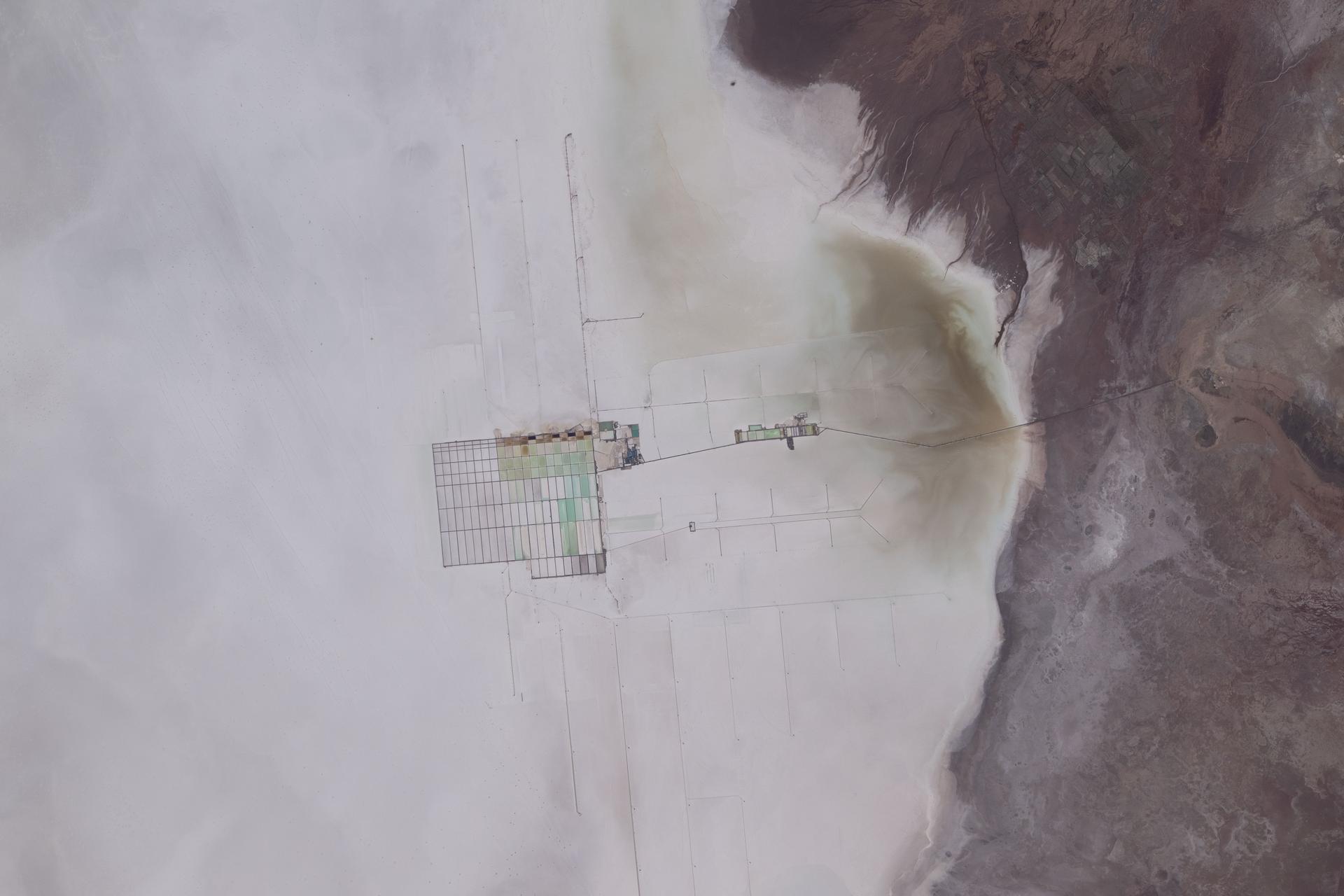 The Salar de Uyuni in Bolivia is the world's largest salt flat and one of the flattest surfaces on Earth. At the center of the photograph is a mining operation extracting extensive lithium deposits across the salt flat.