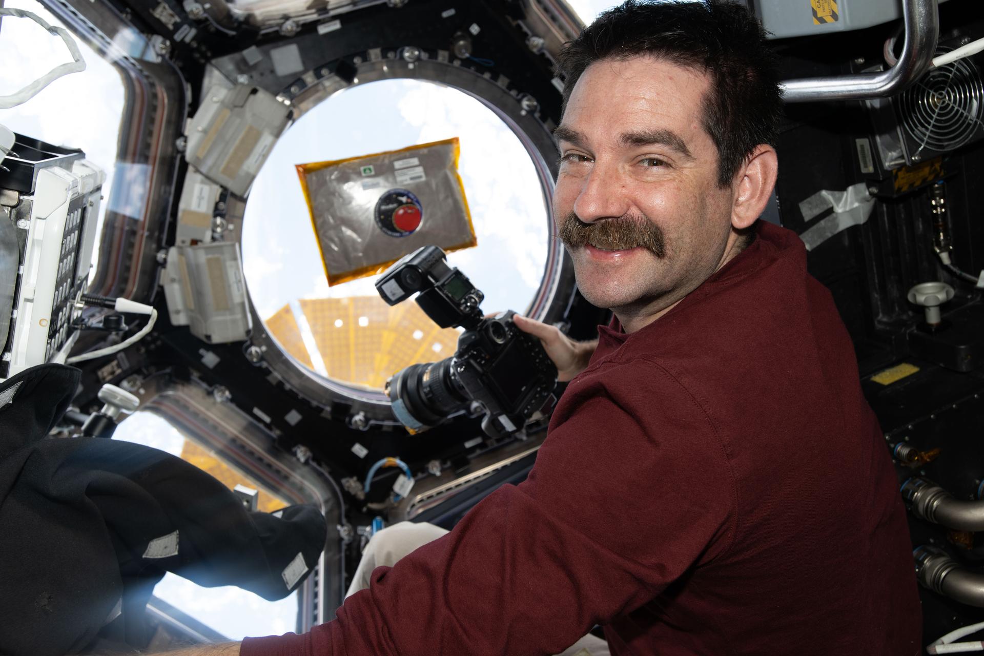NASA astronaut and Expedition 74 flight engineer Jack Hathaway smiles for a portrait inside the International Space Station’s cupola while photographing a sample chamber for the Rhodium Biomanufacturing 03 biotechnology experiment. The investigation uses living systems such as microorganisms and cell cultures to produce materials and biomolecules on a commercial scale. Results may support the production of food, pharmaceuticals, and other materials during long‑duration spaceflight.