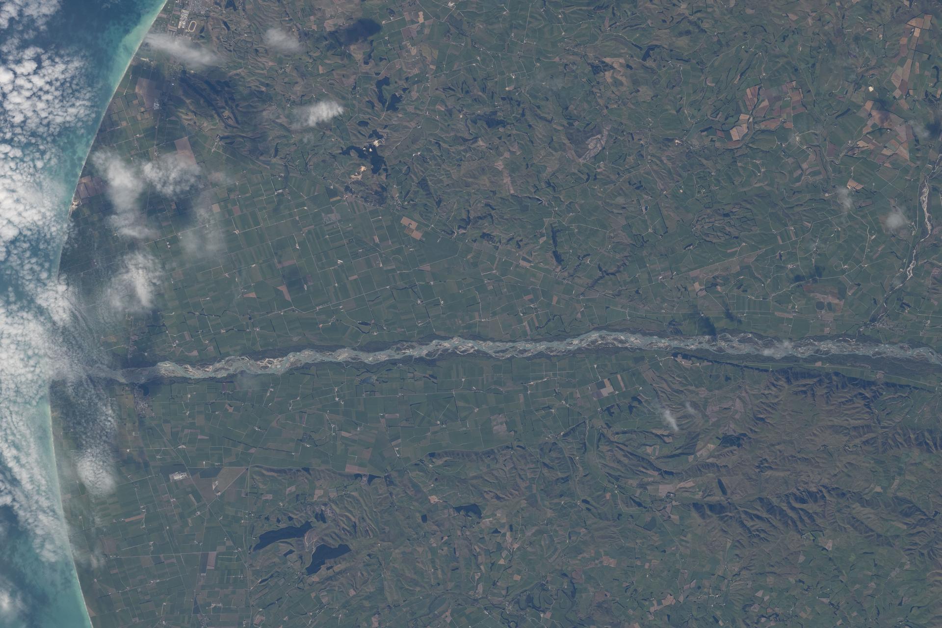 The Waitaki River separates New Zealand’s Otago Region (top) from the Canterbury Region (bottom) along the nation’s South Pacific coast. The Waitaki is fed by glacial lakes, flows through three major hydroelectric lakes, and anchors one of New Zealand’s largest hydroelectric networks. The coastal area surrounding the river is flat, fertile, and ideal for farming.