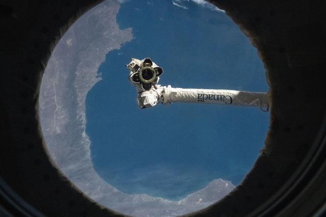 NASA image: The Canadarm2 robotic arm is pictured from a window on the International Space Station