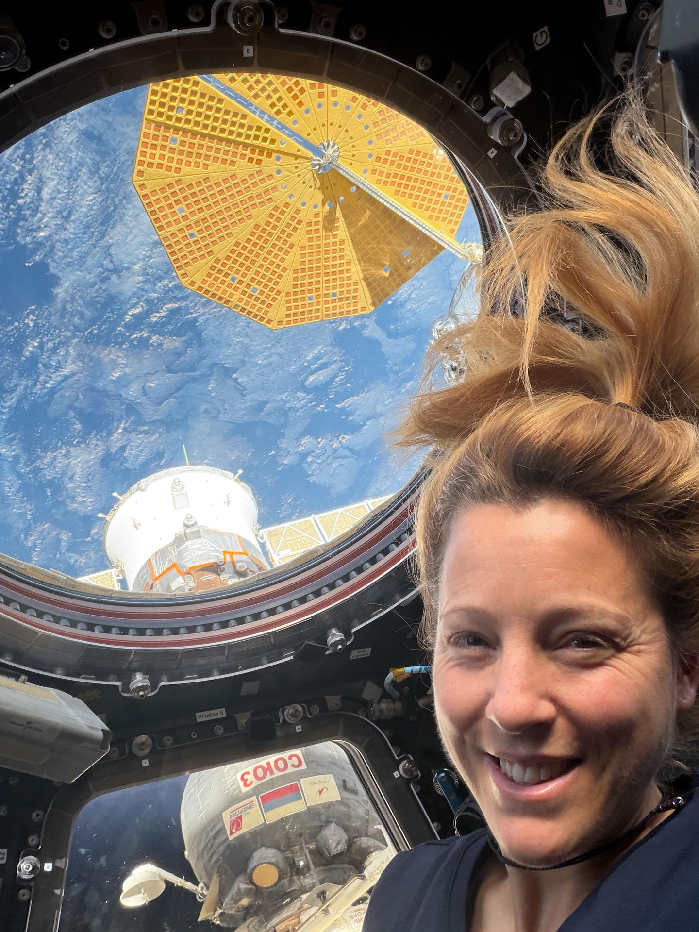 ESA (European Space Agency) astronaut and Expedition 74 flight engineer Sophie Adenot poses for a portrait inside the International Space Station’s cupola. Outside the window are the Soyuz MS‑28 crew spacecraft and a cymbal‑shaped UltraFlex solar array belonging to Northrop Grumman’s Cygnus XL cargo spacecraft. The orbital outpost was soaring 264 miles above the South Atlantic Ocean at the time of this photograph.