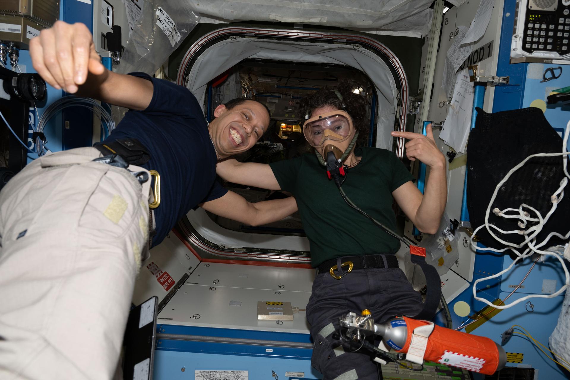 NASA astronauts Chris Williams and Jessica Meir, both Expedition 74 flight engineers, pose for a portrait aboard the International Space Station. Meir is wearing a portable breathing apparatus to test its readiness for unlikely emergency scenarios such as an oxygen leak, chemical leak, or fire aboard the orbital outpost.