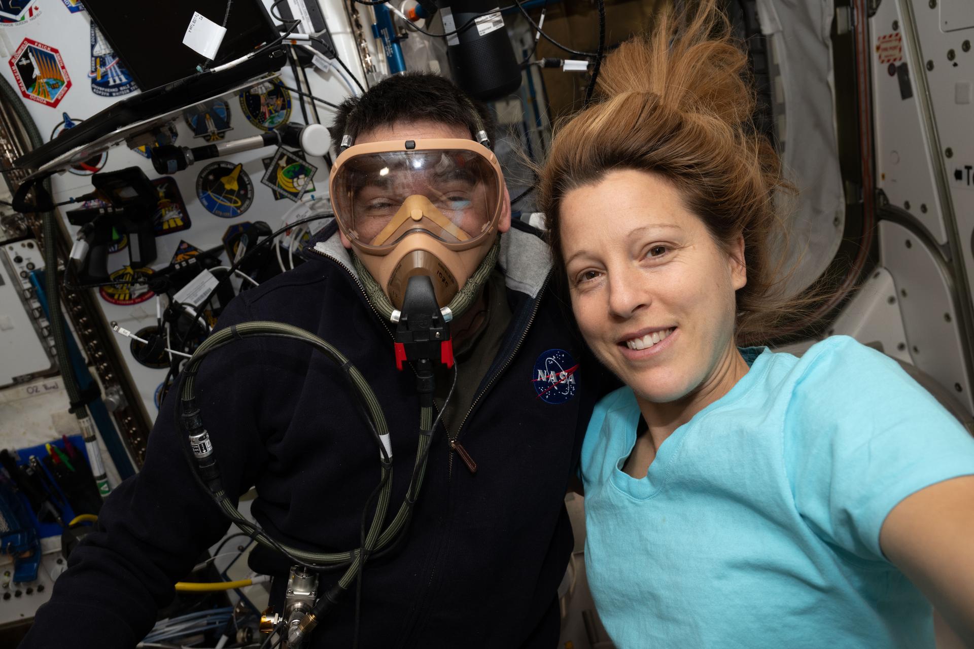 Expedition 74 flight engineers Jack Hathaway of NASA and Sophie Adenot of ESA (European Space Agency) pose for a portrait aboard the International Space Station. Hathaway is wearing a portable breathing apparatus to test its readiness for unlikely emergency scenarios such as an oxygen leak, chemical leak, or fire aboard the orbital outpost.