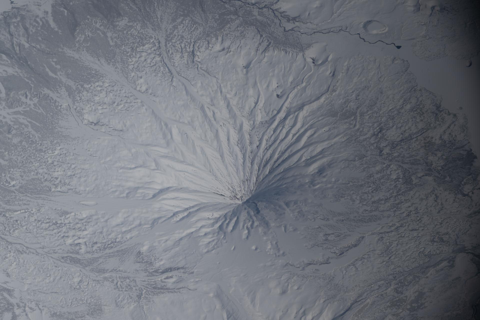 iss074e0454554 (April 10, 2026) --- The snow‑covered Kronotsky, a major stratovolcano on the Kamchatka Peninsula in Russia, is pictured from the International Space Station as it orbited 267 miles above the Pacific Ocean. Kronotsky is known for its picturesque, near‑perfect symmetry, comparable to Japan’s Mount Fuji. Credit: NASA/Chris Williams