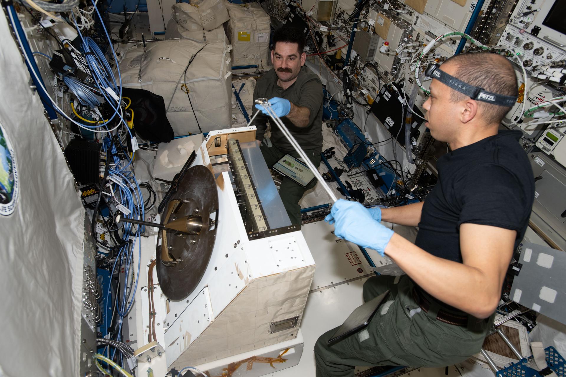 NASA astronauts Jack Hathaway and Chris Williams, both Expedition 74 flight engineers, prepare the NanoRacks External Platform—carrying three scientific payloads—for installation inside the Kibo laboratory module’s airlock where it will be placed outside in the vacuum of space. The payloads will test ultra‑high‑resolution hyperspectral imagery, measure radio signals passing through Earth’s ionosphere, and help doctors identify space‑sensitive proteins while evaluating mobility and neuromuscular health therapies.