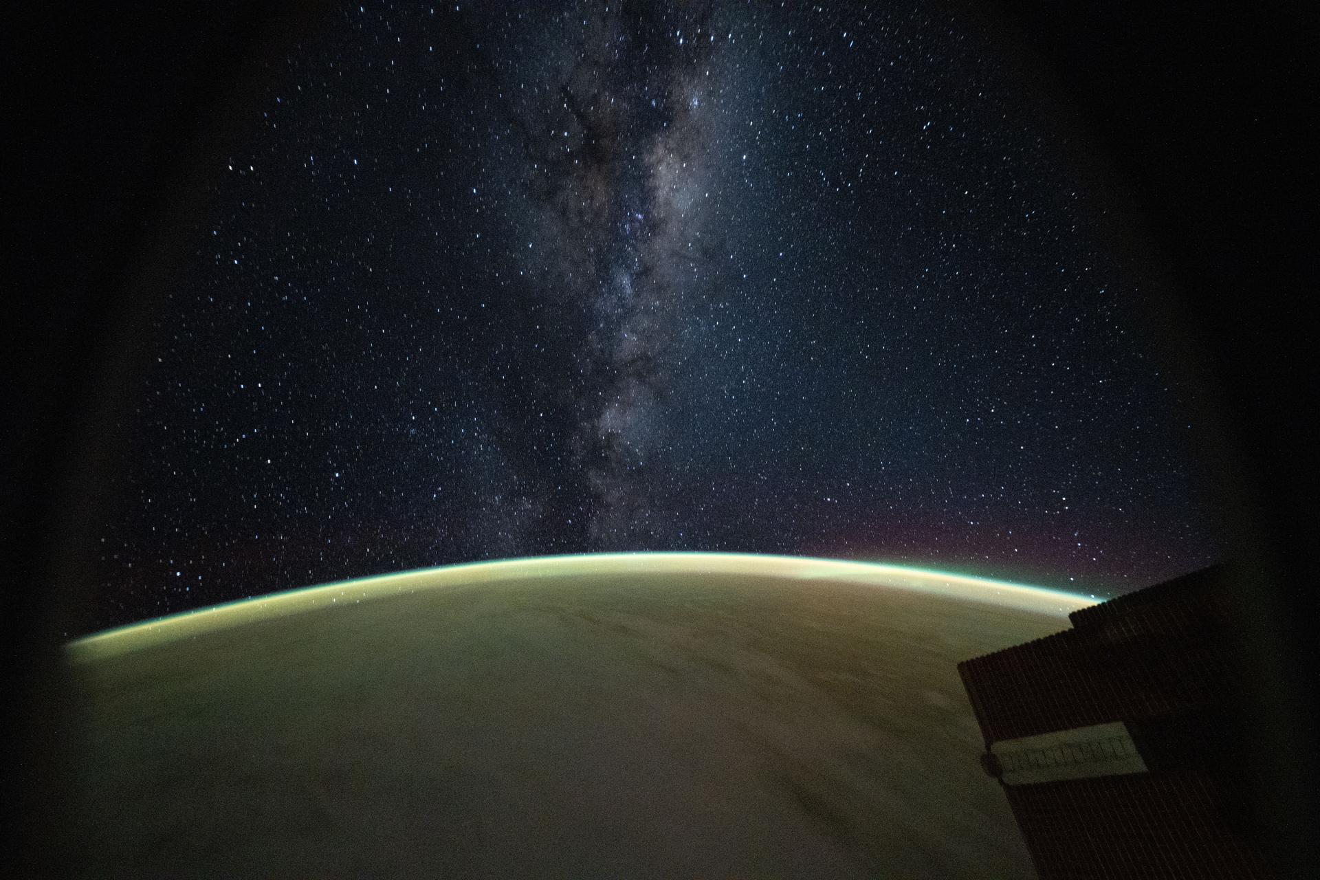 This celestial image captured from a window on a SpaceX Dragon spacecraft docked to the International Space Station highlights the Milky Way rising above Earth's atmospheric glow.