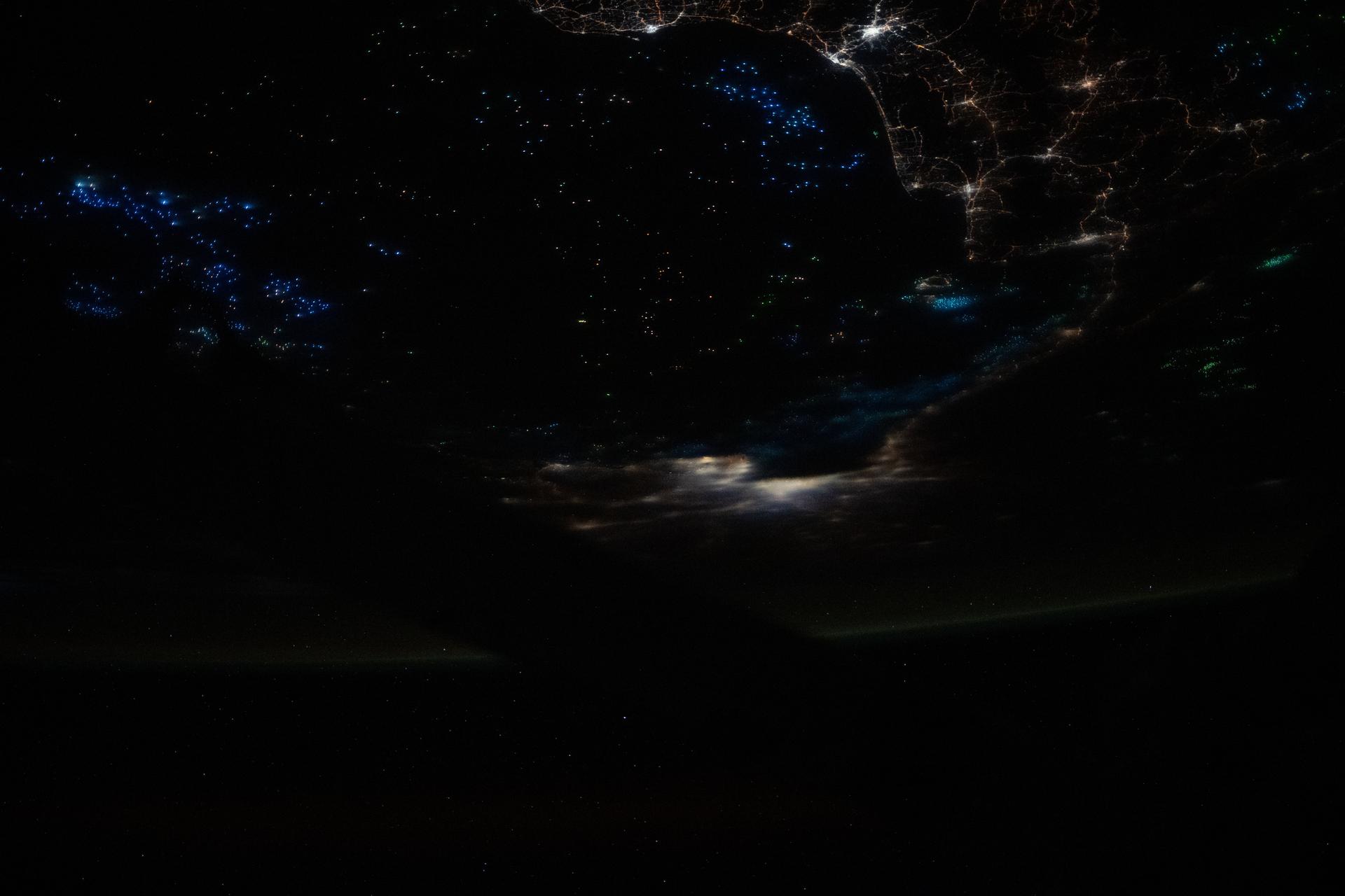 he blue lights of fishing boats dot the Gulf of Thailand in this photograph taken at approximately 12:59 a.m. local time from the International Space Station as it orbited 259 miles above Earth. The lights attract and illuminate plankton and small fish, luring squid toward the boats’ fishing nets. The city lights of Bangkok, Thailand (center), are partially muted by cloud cover.