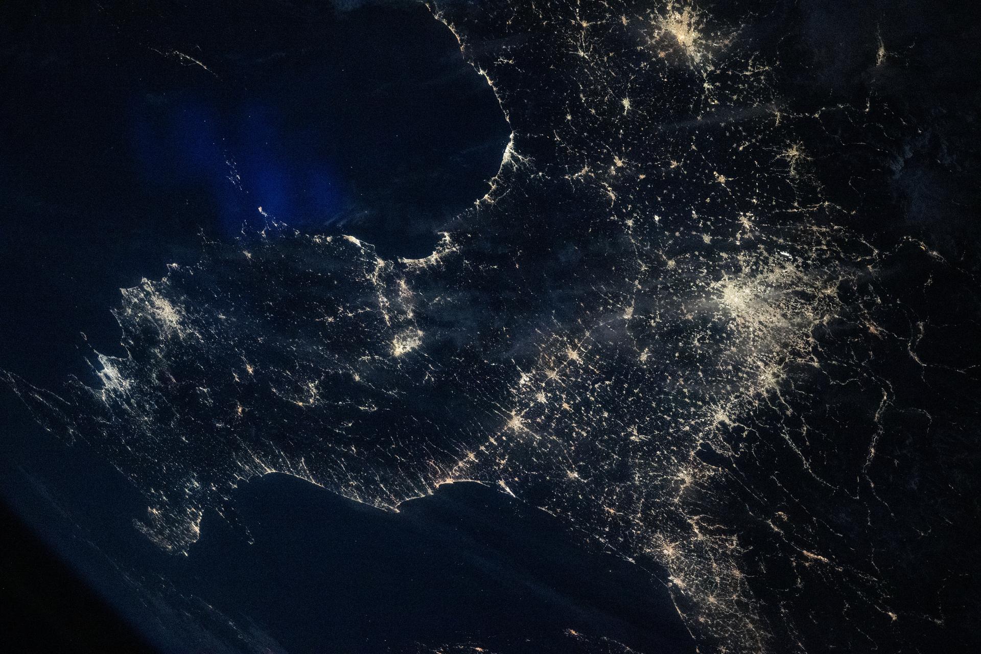 Italy’s darkened Po Valley contrasts with the brighter city lights that surround the region, even though it is one of the most densely populated and industrialized areas in Europe. The Po Valley appears darker from space due to wide expanses of farmland and nearby mountainous terrain that absorb light, creating an overall dimmer appearance.