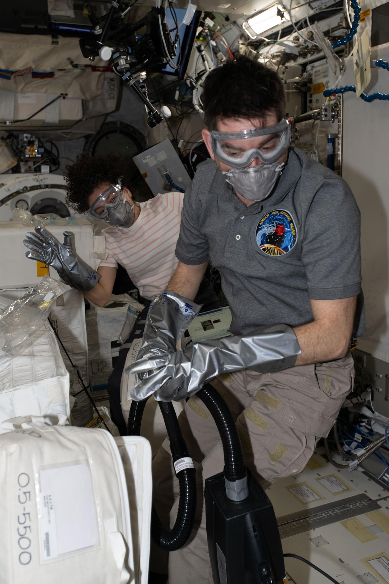 NASA astronauts Jessica Meir and Jack Hathaway, both Expedition 74 flight engineers, wear disposable gloves, dust masks, and safety goggles, as part of standard safety protocol, while unpacking temperature‑controlled scientific samples from a SpaceX Dragon cargo spacecraft and stowing them inside research facilities located aboard the International Space Station’s Kibo laboratory module.