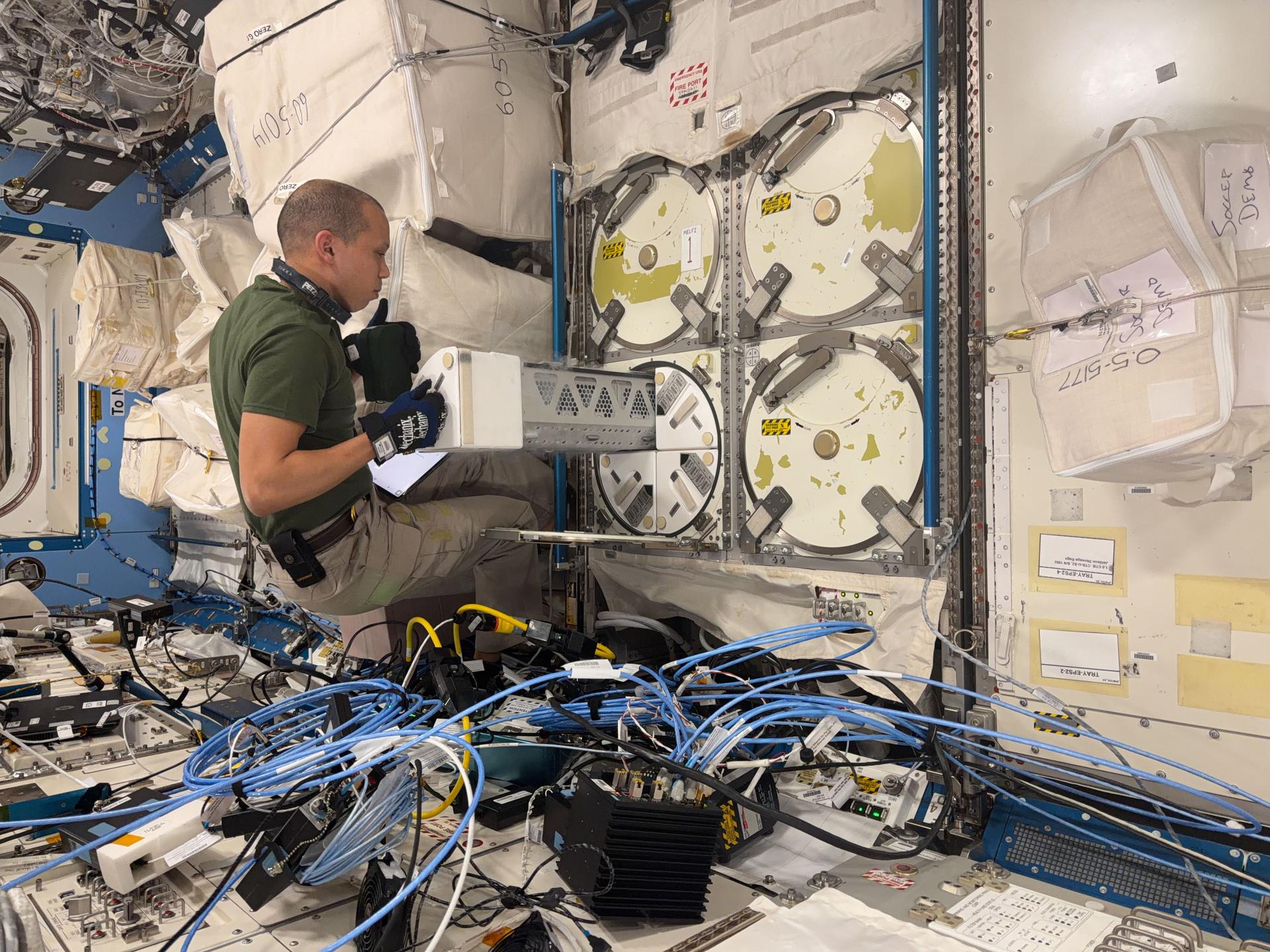 NASA astronaut and Expedition 74 flight engineer Chris Williams inserts a cryogenic storage unit, called a dewar, into a science freezer aboard the International Space Station’s Kibo laboratory module. Earlier, Williams had loaded the dewar with ice bricks that help keep scientific samples extremely cold inside the ultra‑cold freezer, known as the Minus Eighty‑Degree Laboratory Freezer for the International Space Station, or MELFI.