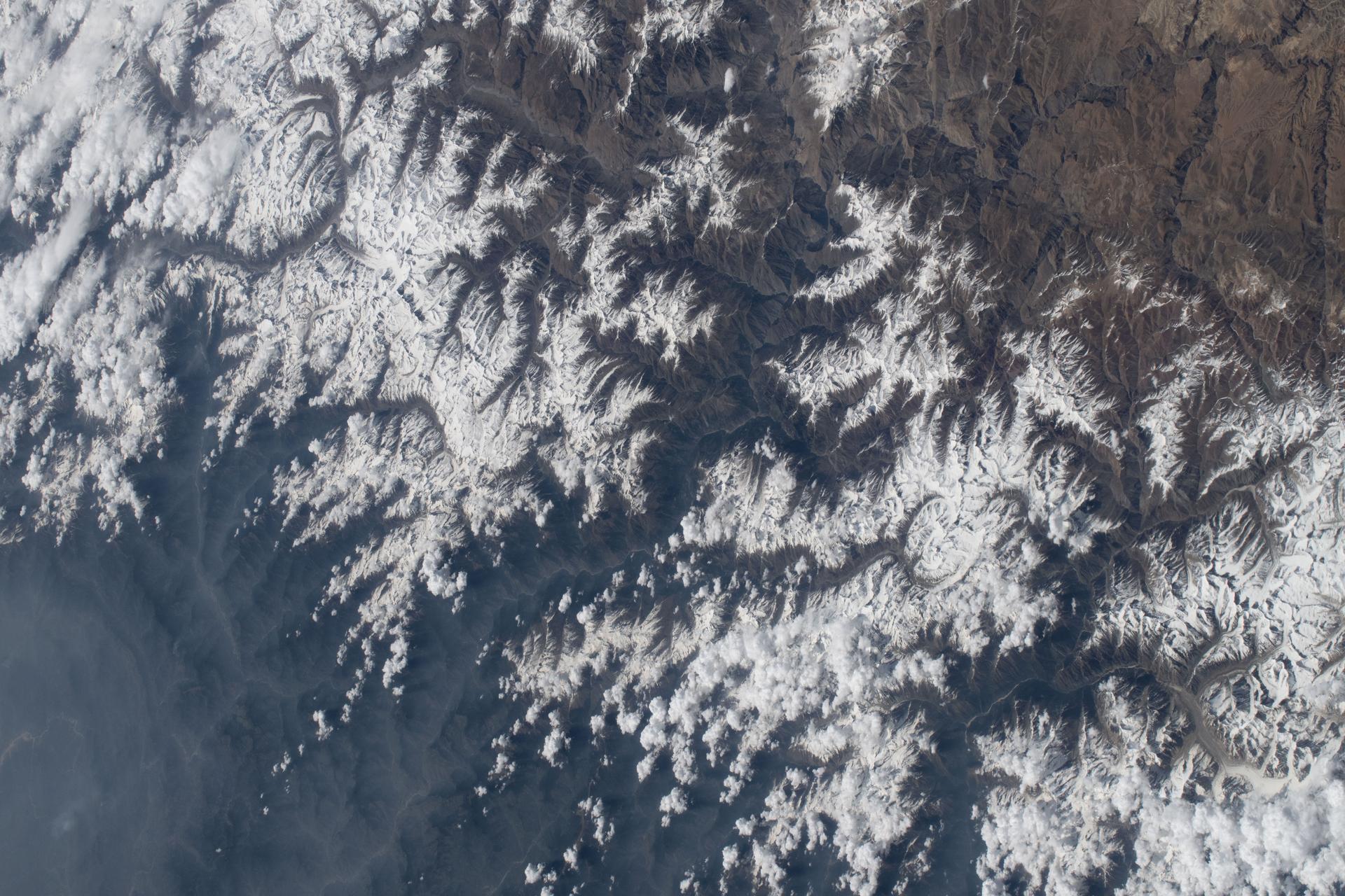 The snow‑capped Himalayas separate Nepal from China in this photograph from the International Space Station as it orbited 259 miles above the Asian mountain range. The range acts as a climate barrier, trapping cooler, moisture‑laden air on the Nepal side and creating a sharp contrast between Nepal’s lush forests and the much drier Tibetan Plateau to the north.