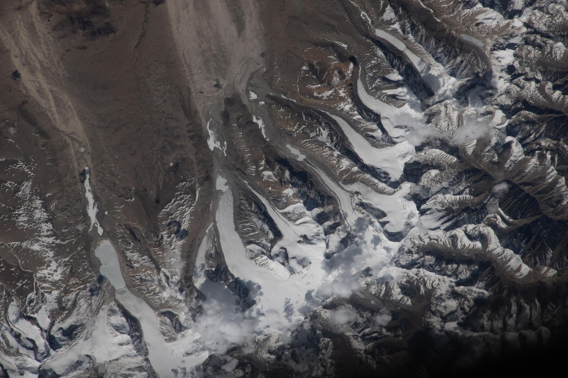 The Himalayas separate Nepal from China in this photograph from the International Space Station as it orbited 259 miles above the western Tibetan Plateau. Glaciers—slow‑moving rivers of ice that carve paths into mountainsides—flow downhill from the Himalayas’ northern slopes onto China's Tibetan Plateau.