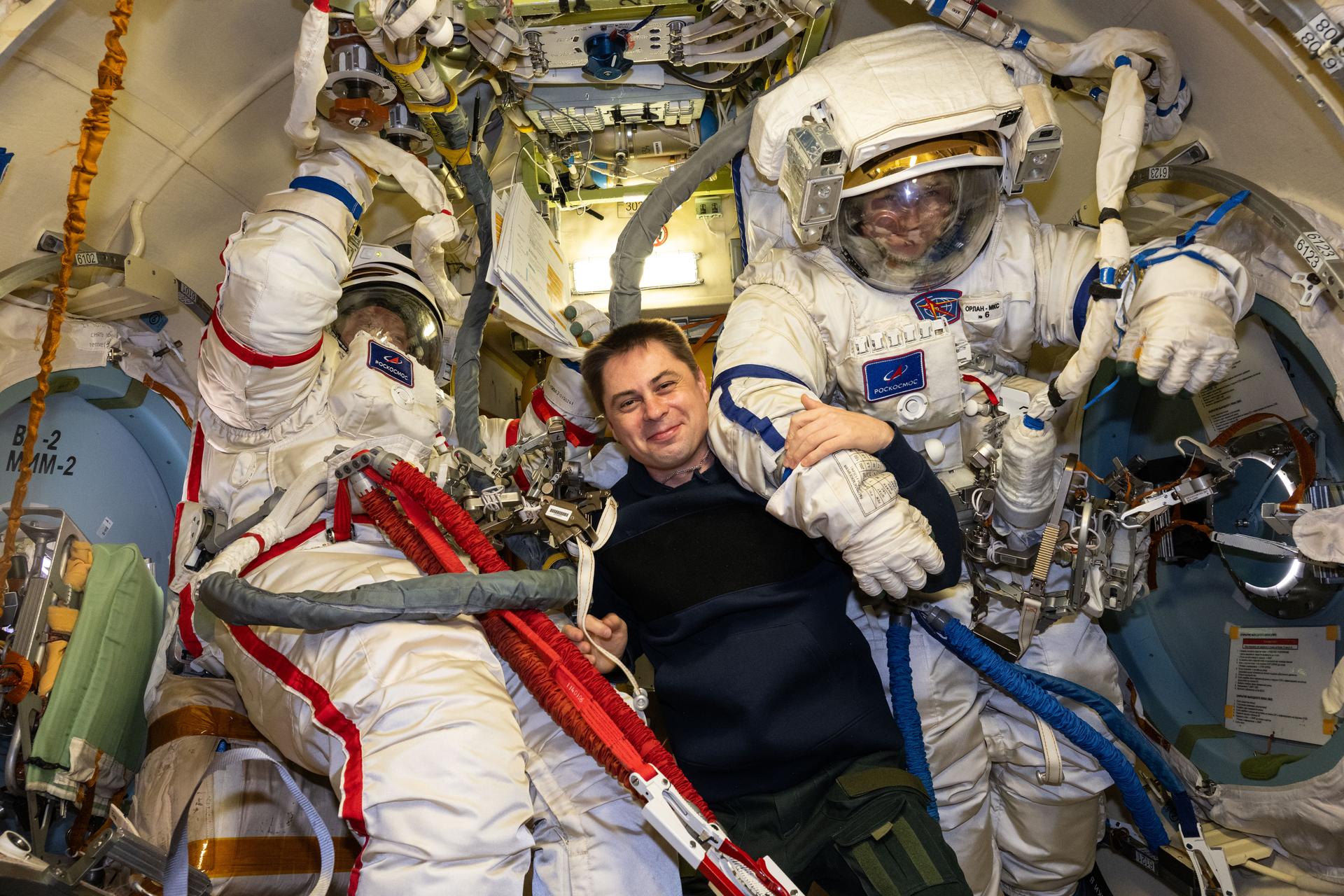 Roscosmos cosmonauts Sergey Kud-Sverchkov (left) and Sergei Mikaev (right), Expedition 74 commander and flight engineer respectively, are pictured inside the Poisk module's airlock trying on their Orlan spacesuits as Roscosmos flight engineer Andrey Fedyaev (center) assists them. The duo was preparing for a spacewalk to install a solar radiation experiment and remove biological exposure hardware on the outside of the International Space Station.