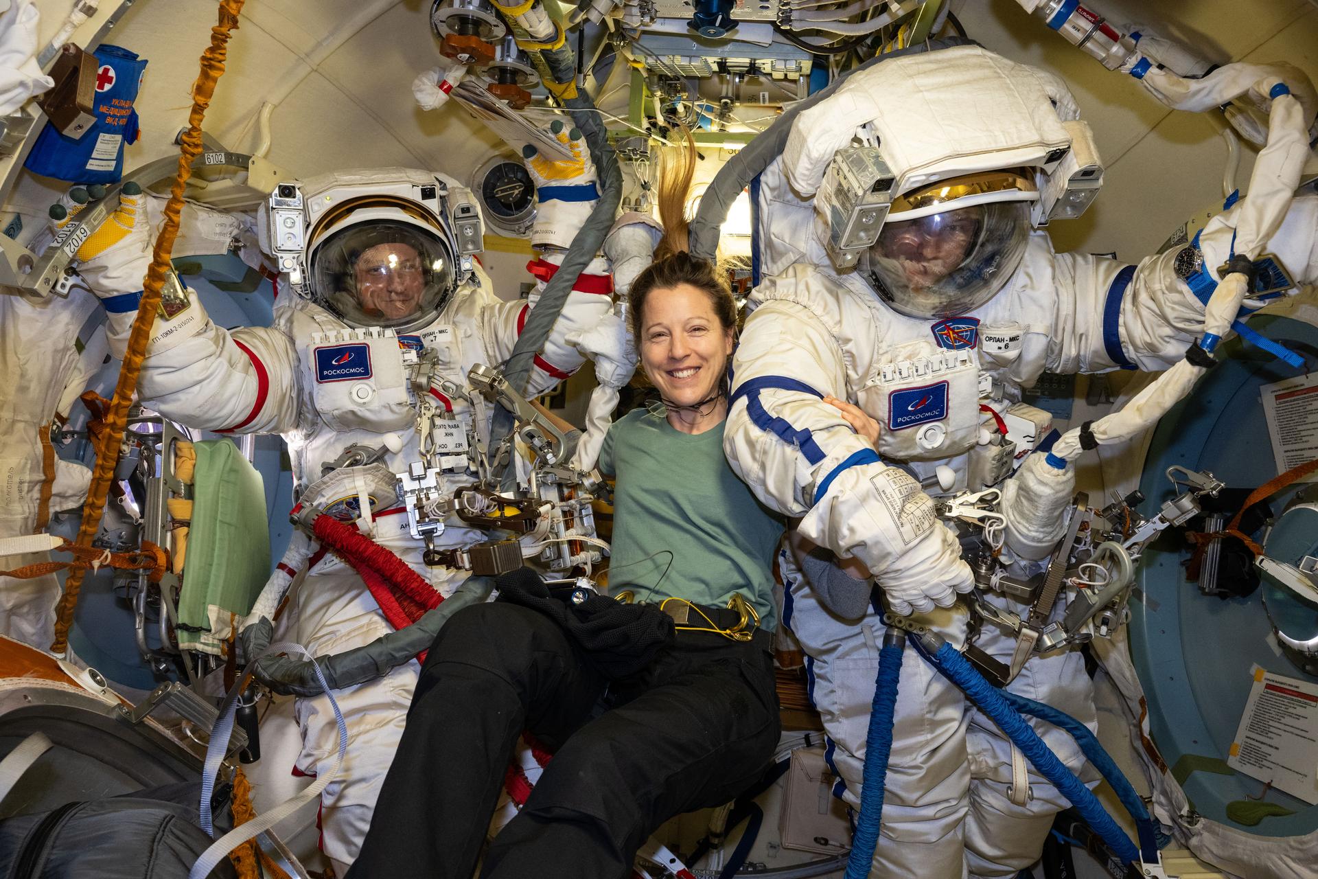 Roscosmos cosmonauts Sergey Kud-Sverchkov (left) and Sergei Mikaev (right), Expedition 74 commander and flight engineer respectively, are pictured inside the Poisk module's airlock trying on their Orlan spacesuits as flight engineer Sophie Adenot of ESA (European Space Agency) assists them. The duo was preparing for a spacewalk to install a solar radiation experiment and remove biological exposure hardware on the outside of the International Space Station.