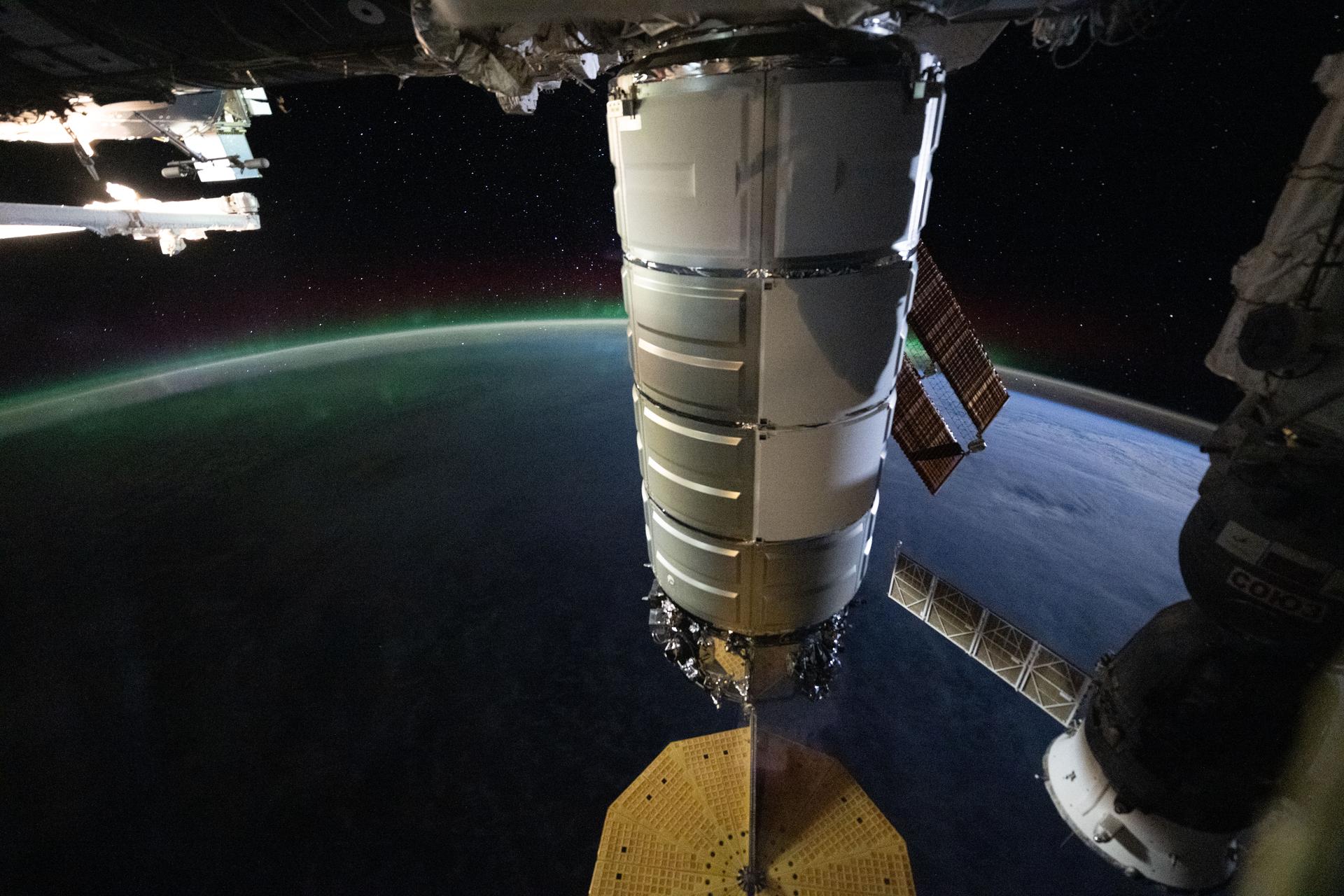 Northrop Grumman's Cygnus XL cargo spacecraft, berthed to the Earth-facing port of the Unity module, is pictured from a window in the International Space Station's cupola. The orbital outpost was soaring 274 miles above the South Indian Ocean east of the French Southern and Antarctic Lands as an aurora australis beamed above Earth's horizon beneath a starry sky.