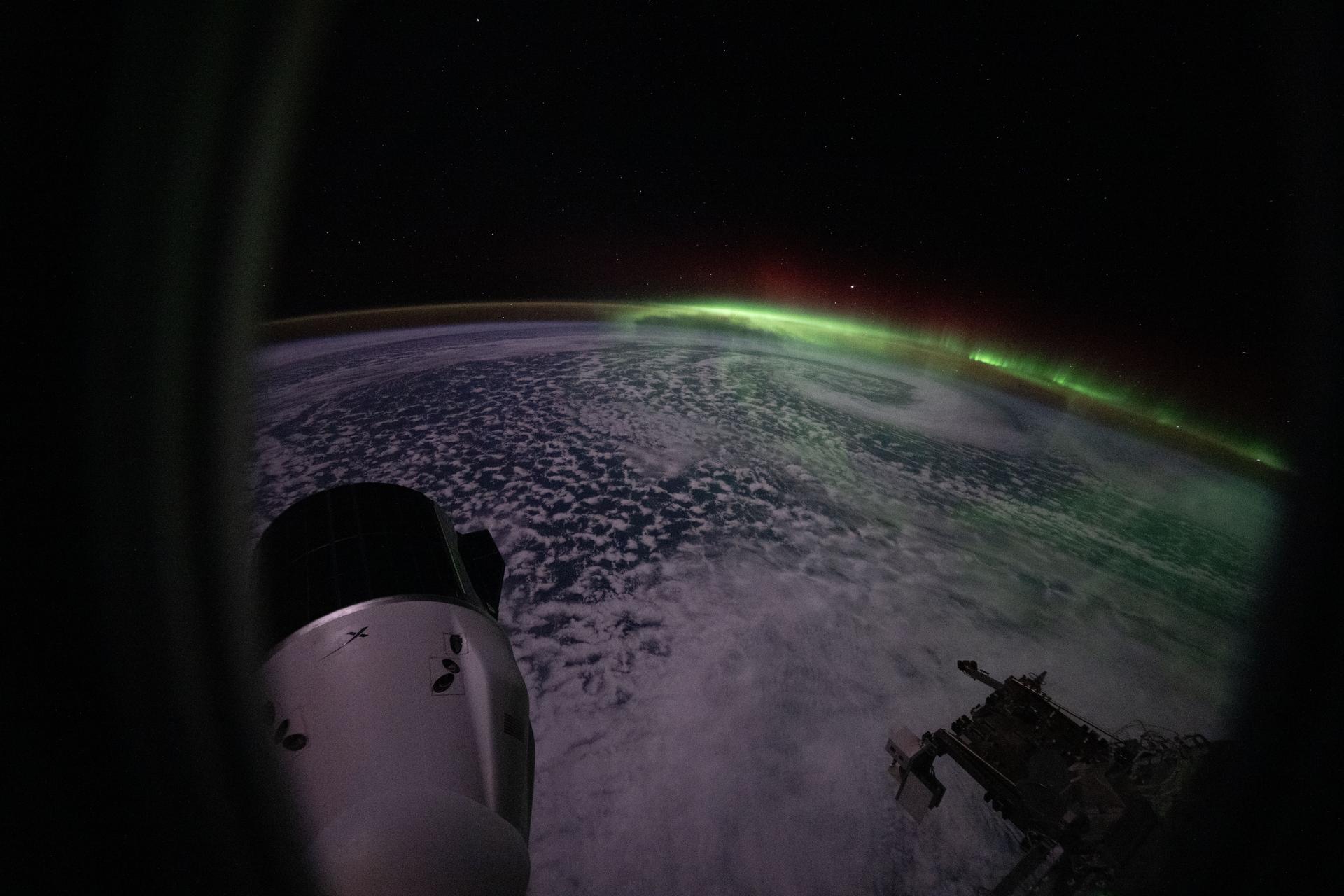 The aurora australis arcs above a swirling cloud formation in this photograph taken from a window on a SpaceX Dragon crew spacecraft docked to the Harmony module's space-facing port on the International Space Station. At lower left is a SpaceX Dragon cargo spacecraft docked to Harmony's forward port. The orbital outpost was soaring 272 miles above the southern Indian Ocean southwest of Perth, Australia, at the time of this photograph.